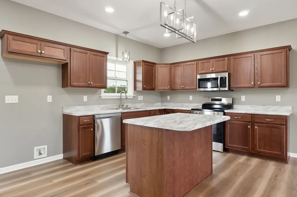 A modern kitchen with cherry wood cabinets, marble countertops, stainless steel appliances, and a central island under elegant pendant lighting.