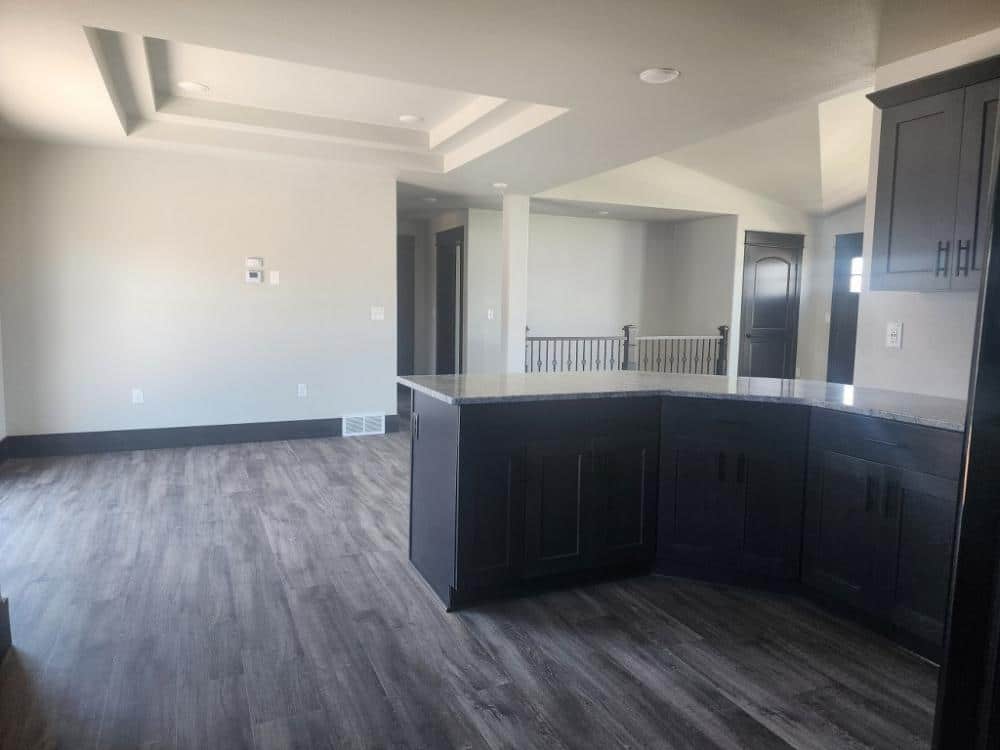 Spacious modern kitchen with dark wooden cabinets, a large central island, light-colored walls, tray ceiling, and sleek wood flooring. Airy and minimalistic.