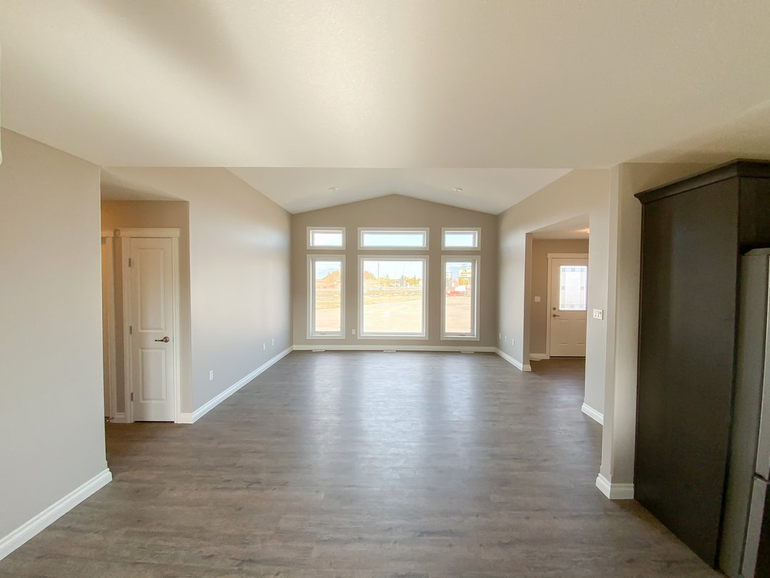 Spacious, empty room with light gray walls and dark wood flooring. Large windows and a door offer natural light. Calm and inviting atmosphere.
