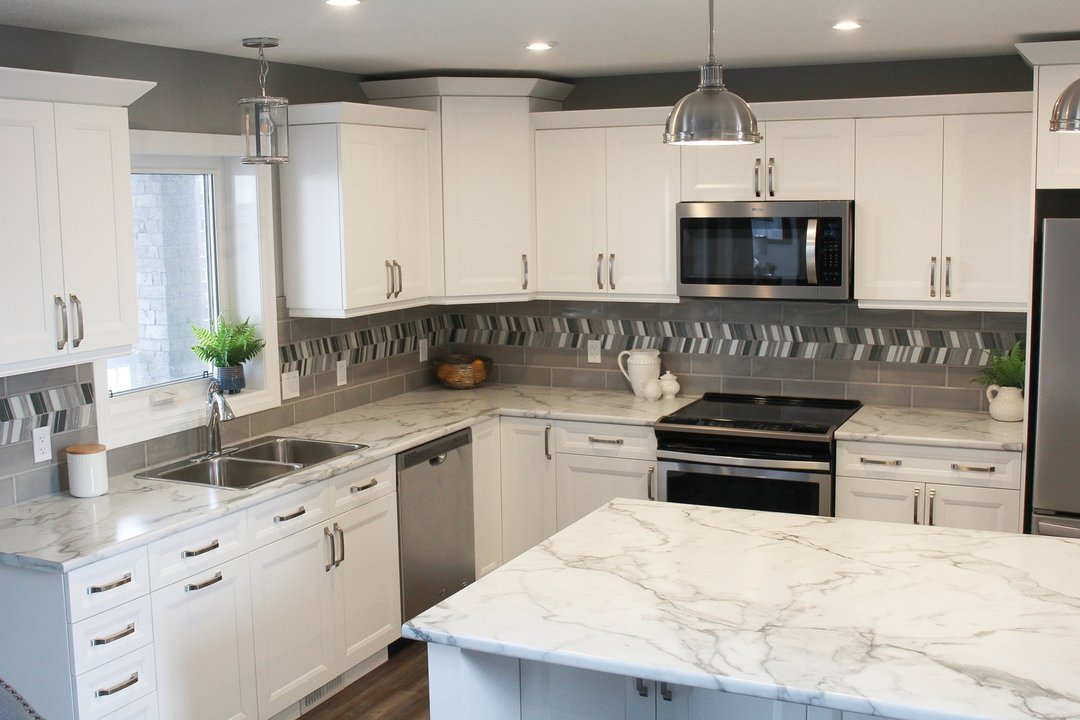 Modern kitchen with white cabinets, marble countertops, and stainless steel appliances. Decor includes potted plants and stylish pendant lights.