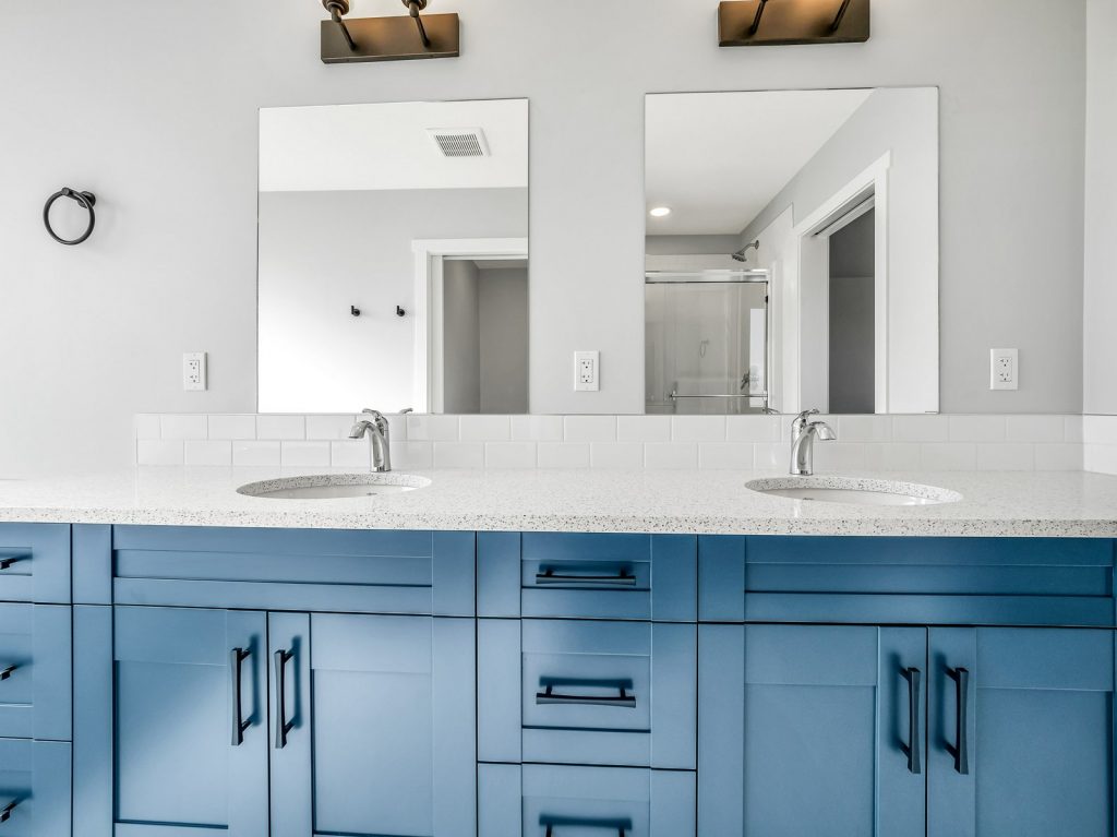 Modern bathroom with blue double vanity and granite countertop. Two mirrors, twin sinks, and a sleek, minimalist design create a clean, fresh look.