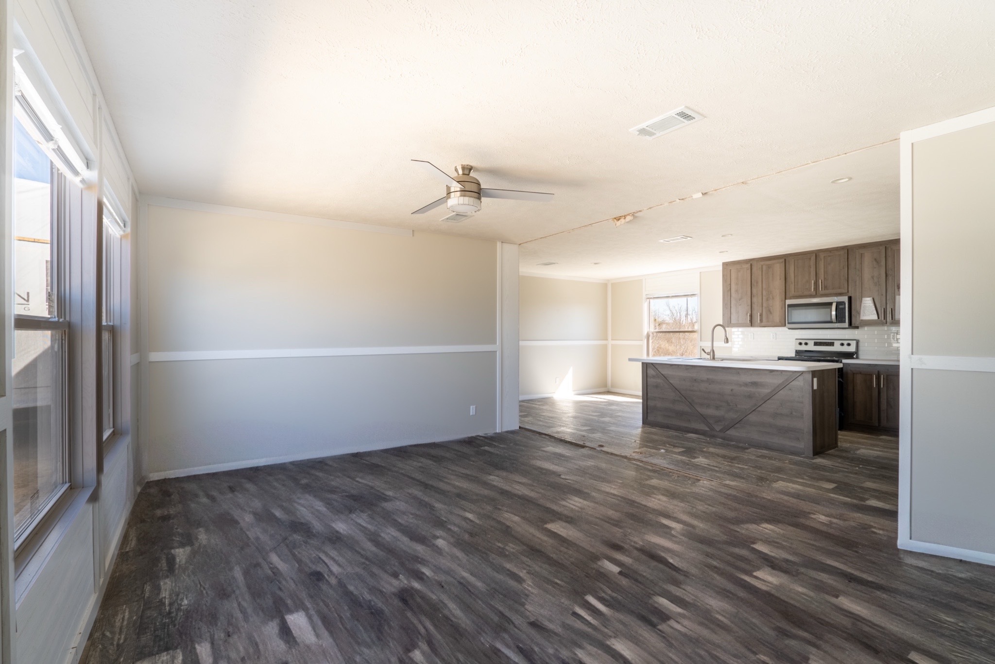 Spacious open-concept room with a modern kitchen. Features light beige walls, dark wood flooring, a ceiling fan, and stainless steel appliances. Bright and airy.