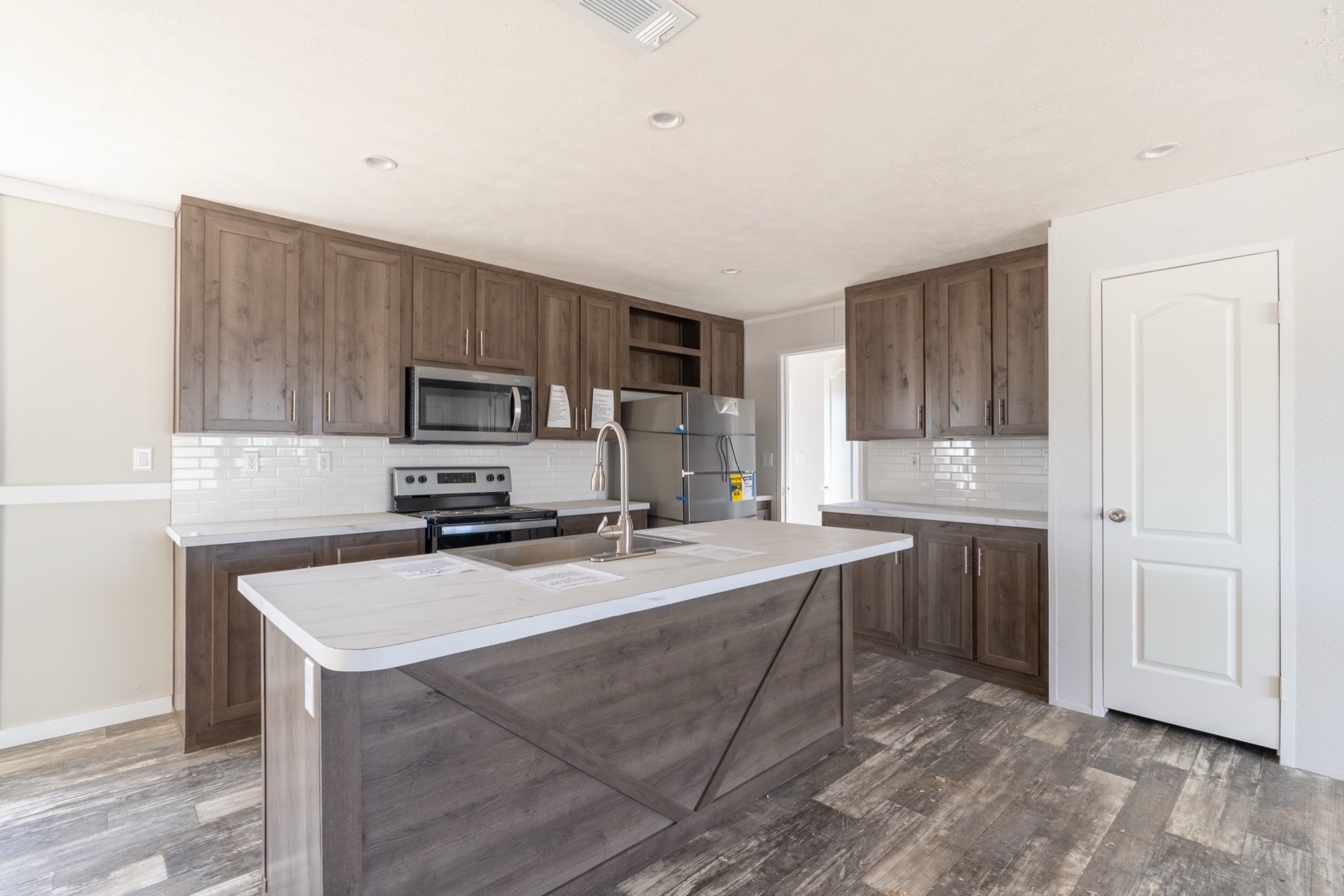 Modern kitchen with dark wood cabinets, white countertops, and stainless steel appliances. Bright lighting and a spacious layout create a welcoming feel.