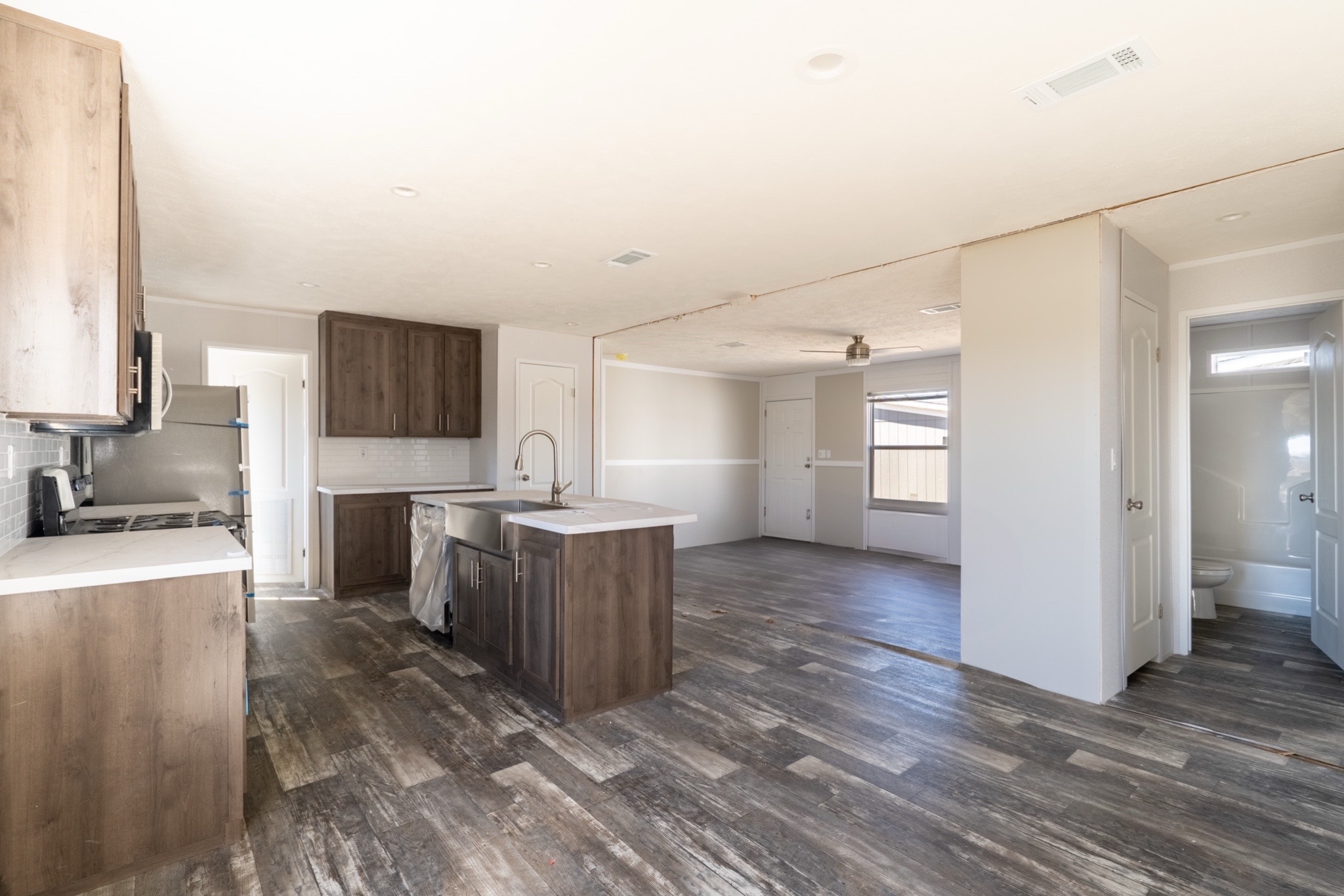 Spacious open-plan kitchen and living area with light walls and rustic wood floors. Features dark wood cabinets, large windows, and an island.
