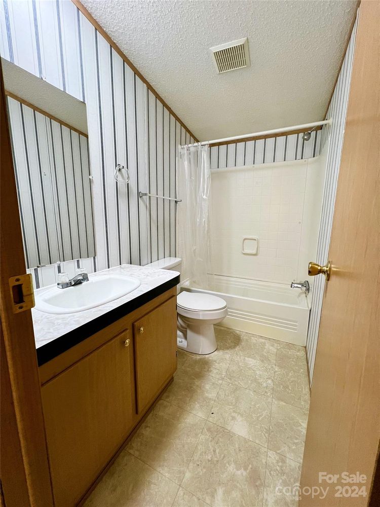 Small bathroom with wood accents, featuring a single sink vanity, striped wallpaper, toilet, and a white bathtub with a shower curtain. Simple and clean.