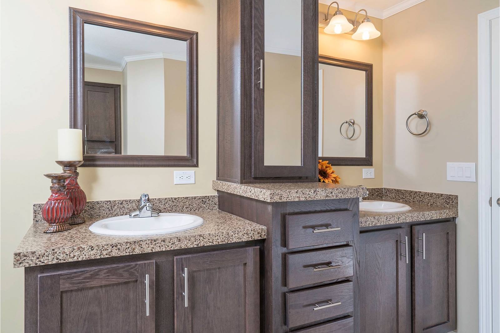 Elegant bathroom with dual sinks, dark wood cabinets, granite countertops, and two large mirrors. Soft lighting and a red vase add warmth.