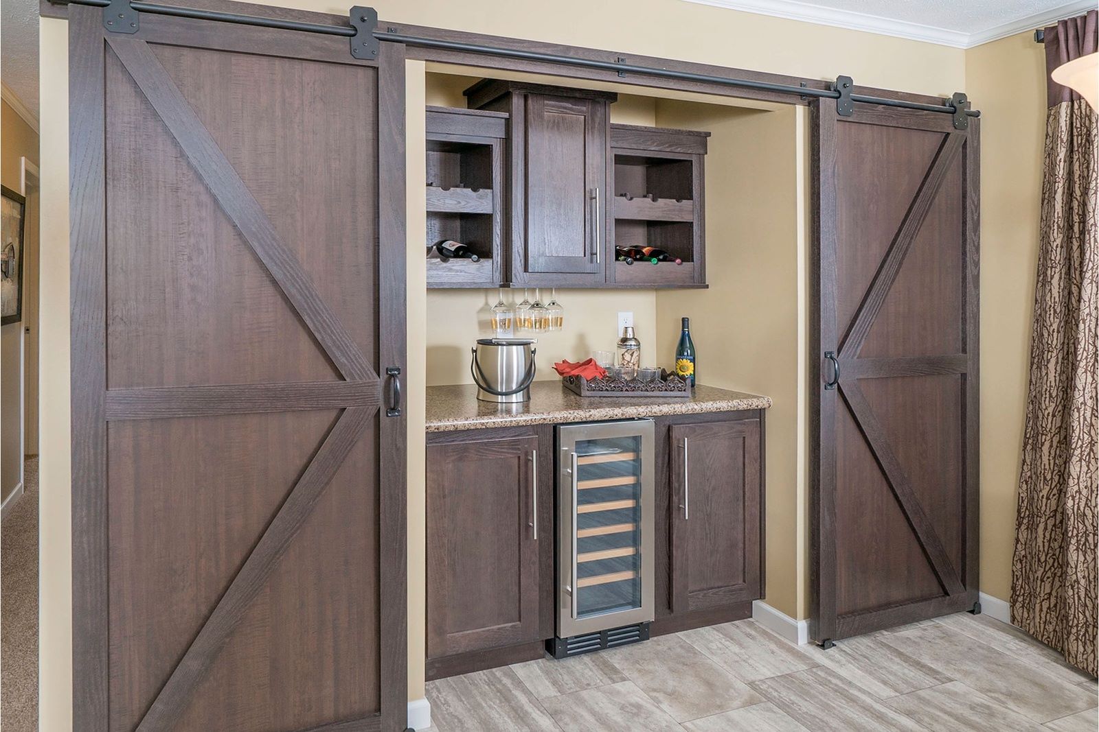 Spacious home bar with dark wood cabinetry, a central wine cooler, and slide-open barn doors. Wine bottles and glasses add a cozy, inviting feel.