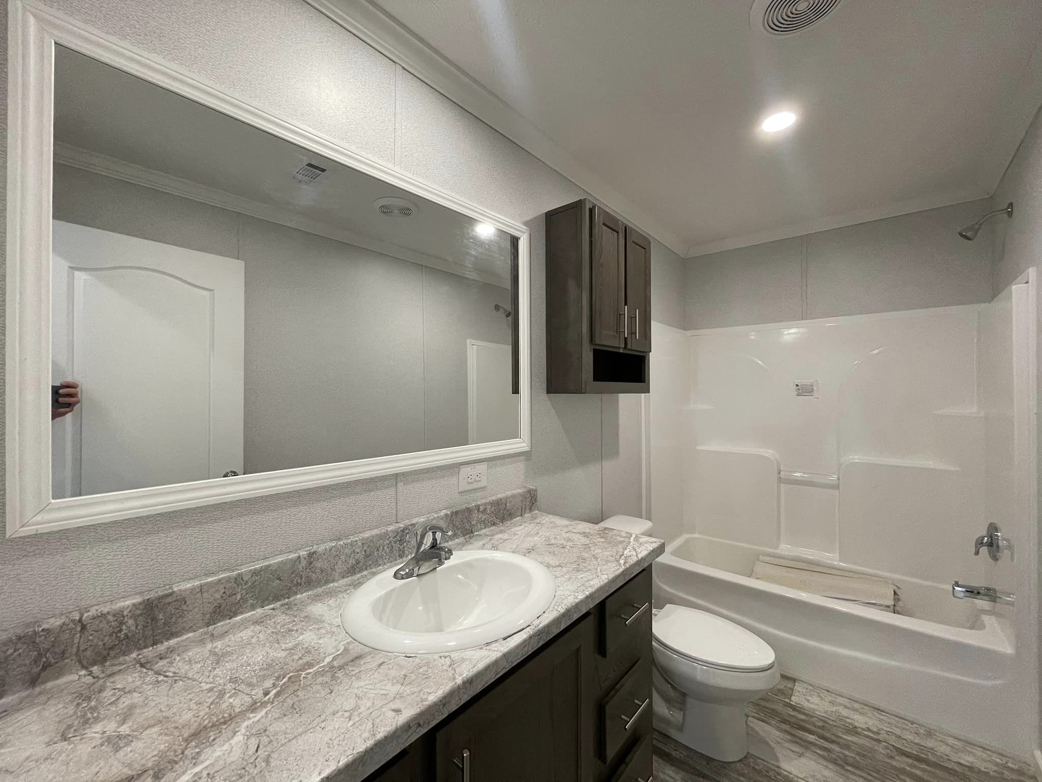 Modern bathroom with neutral tones featuring a marble countertop, white sink, large mirror, dark wood cabinets, bathtub, and toilet under soft lighting.