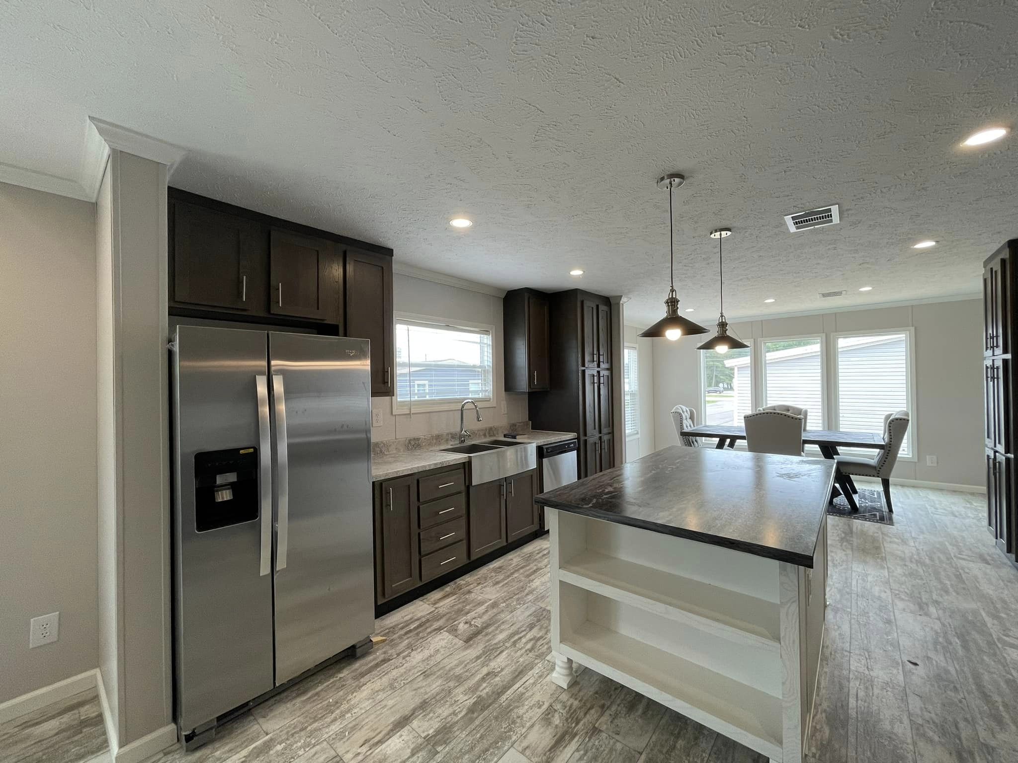 Modern kitchen and dining area with dark wood cabinets, a stainless steel fridge, farm sink, and island. Pendant lights and a dining table create a cozy, elegant ambience.