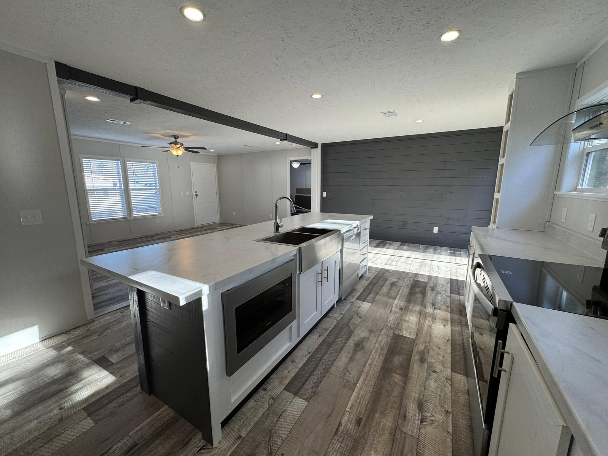 Modern kitchen with sleek white cabinets, marble countertops, and wood flooring. Central island with a sink and built-in appliances. Bright and open space.