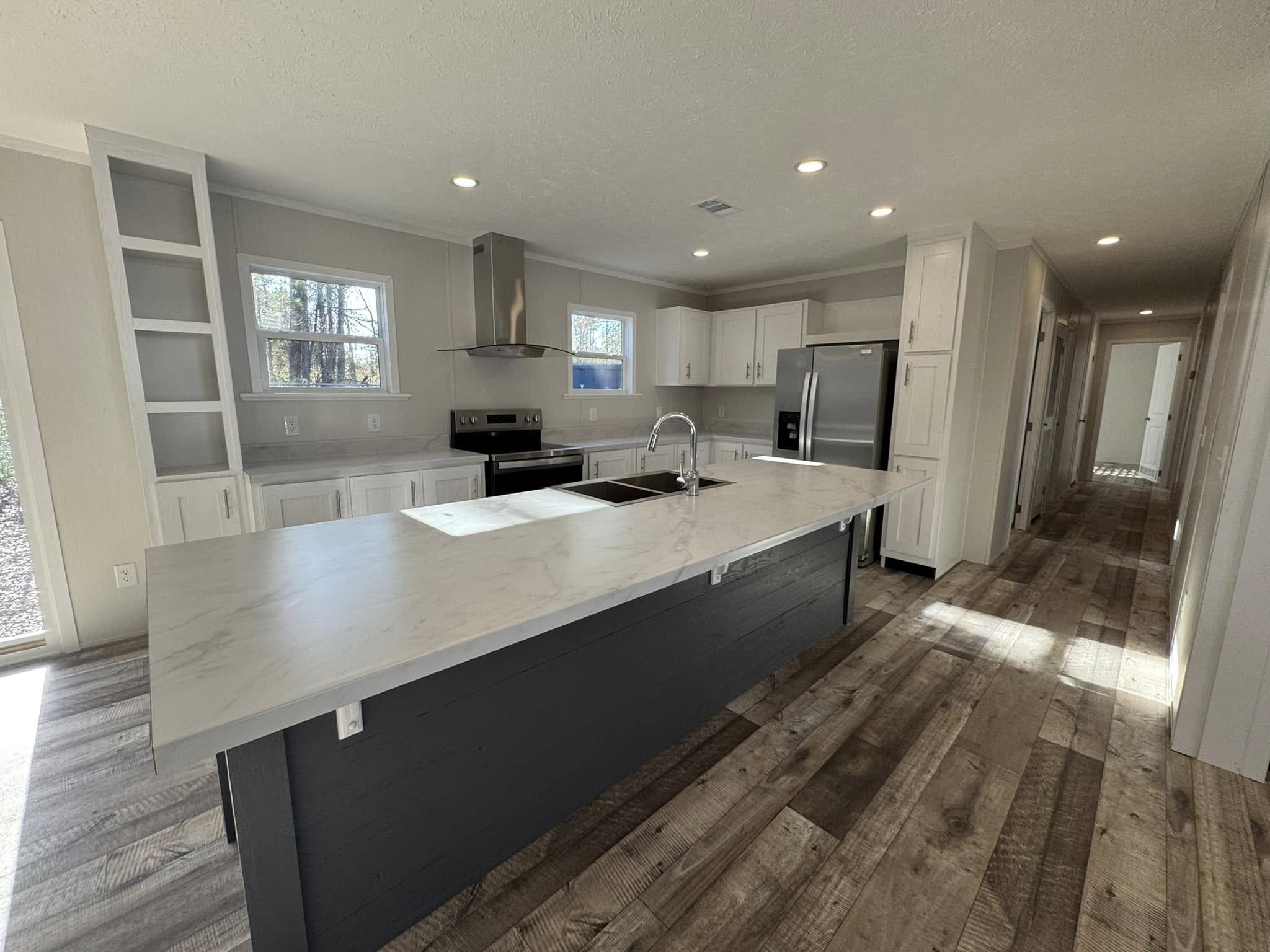 Spacious modern kitchen with white cabinets, a large marble island, stainless steel appliances, and wood flooring, creating a bright, inviting ambiance.