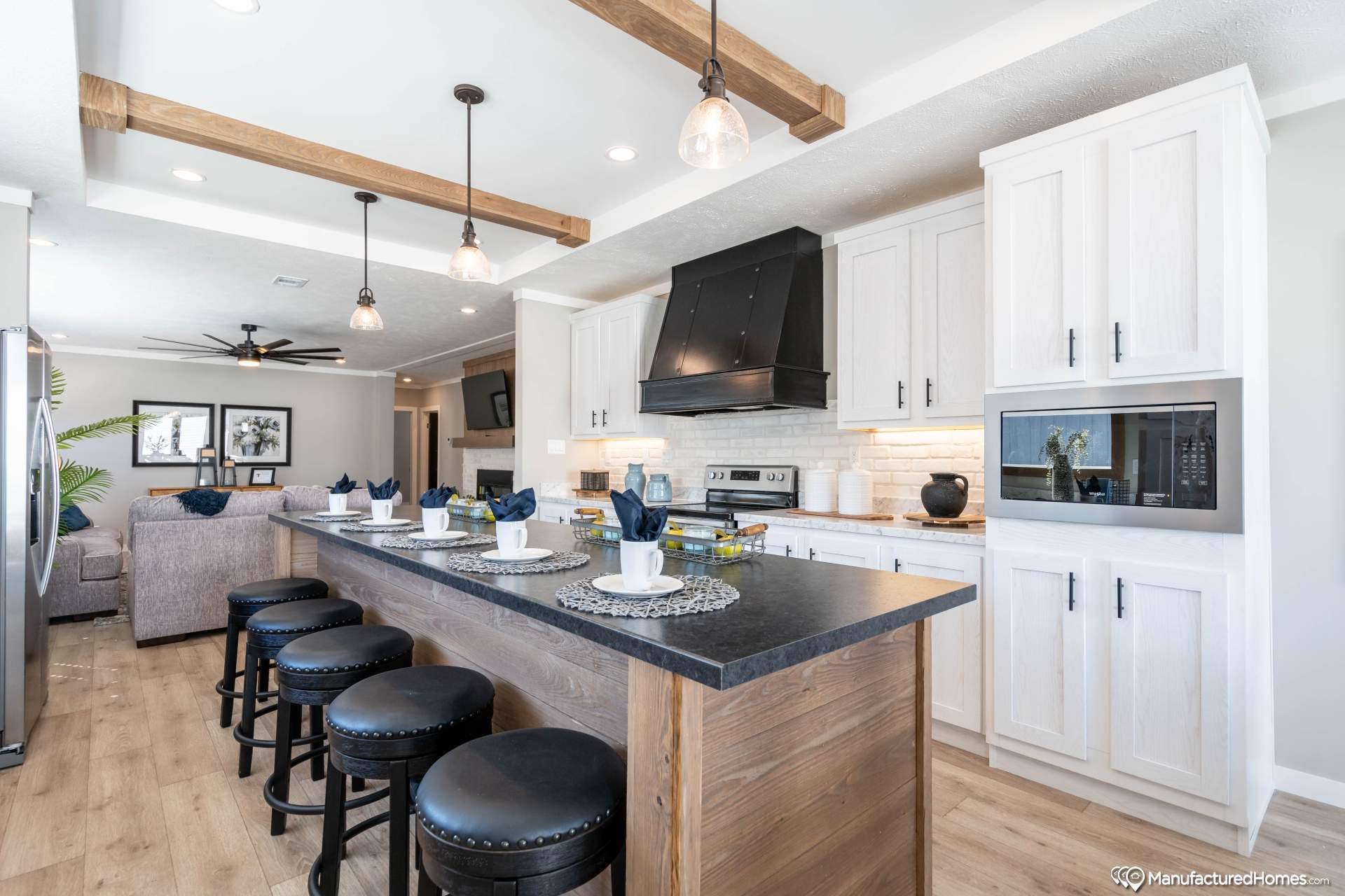 Modern kitchen with a rustic wooden island, black stools, white cabinets, and a black range hood. Pendant lights create a warm, inviting ambiance.