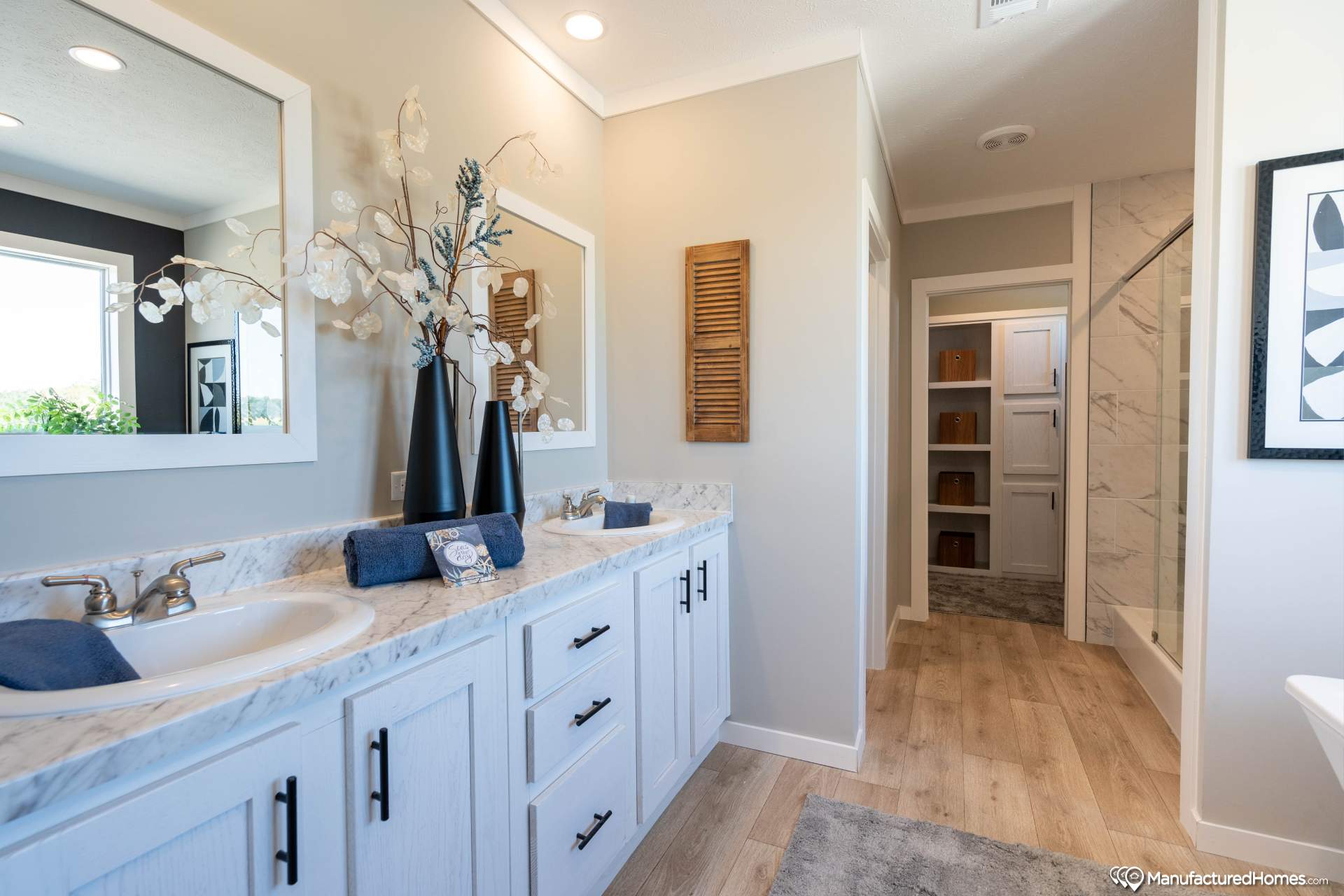 Modern bathroom with dual sinks, framed mirrors, and sleek decor. Features marble countertops, beige walls, and wood accents, creating a serene ambiance.