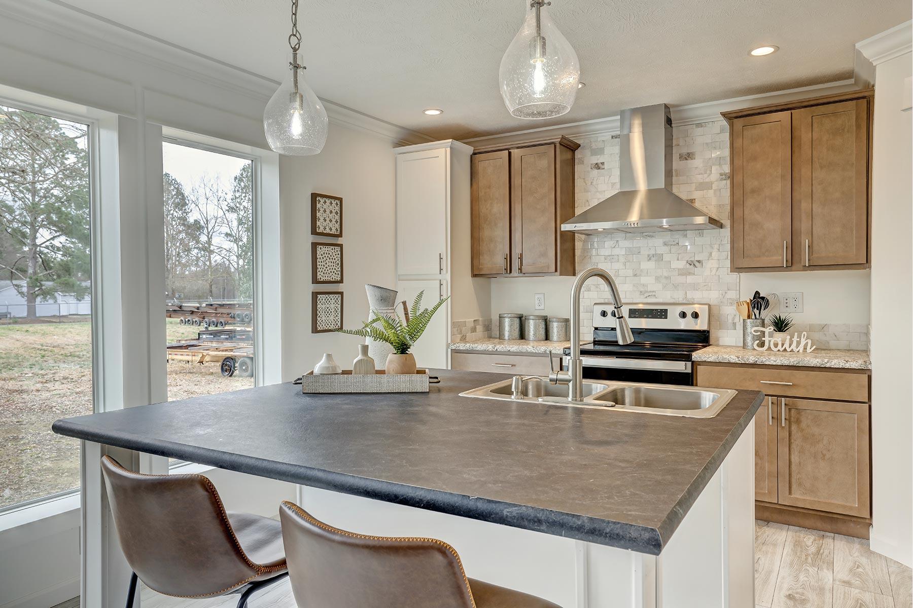Modern kitchen with wood cabinets, stainless steel appliances, and a dark countertop on a central island. Large windows add natural light. Cozy and inviting.