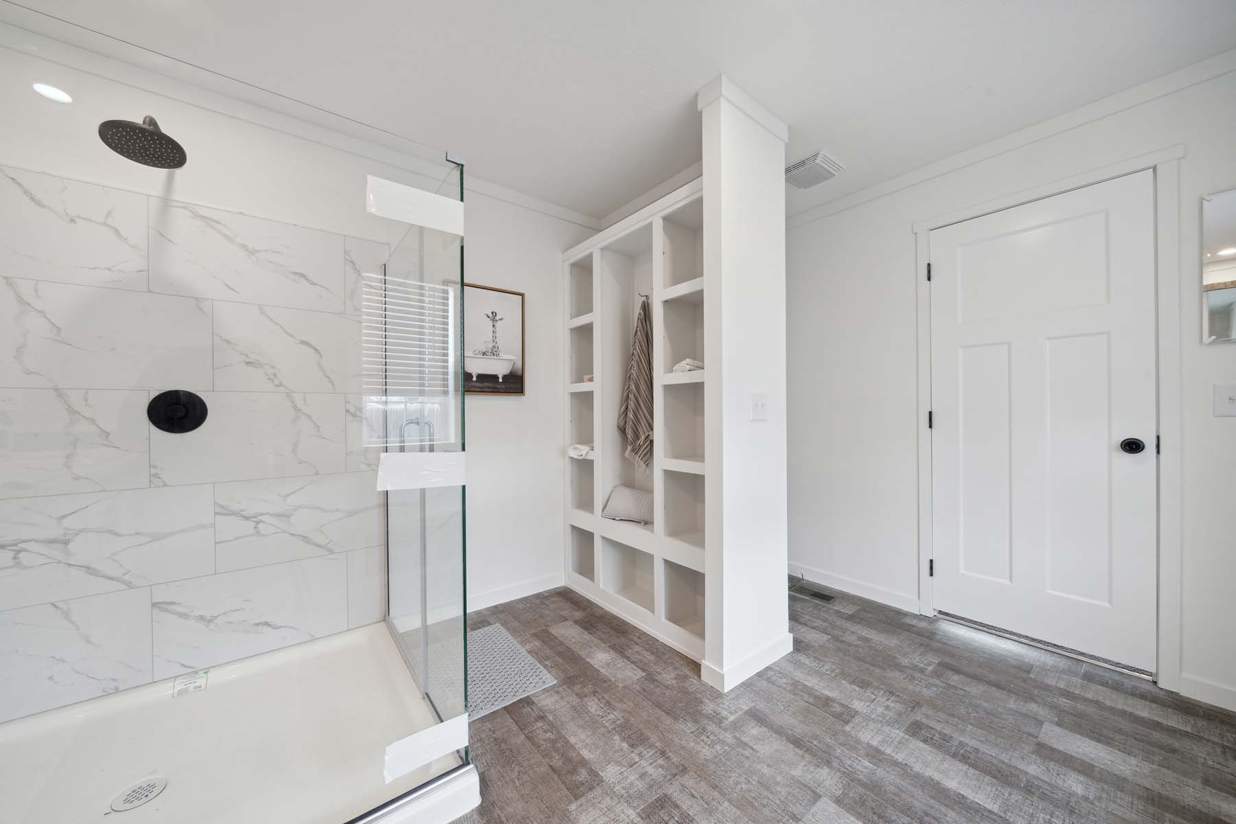 Modern bathroom with glass shower, marble tiles, open shelving with towels, and wood-style flooring. Bright, clean, and minimalist design.