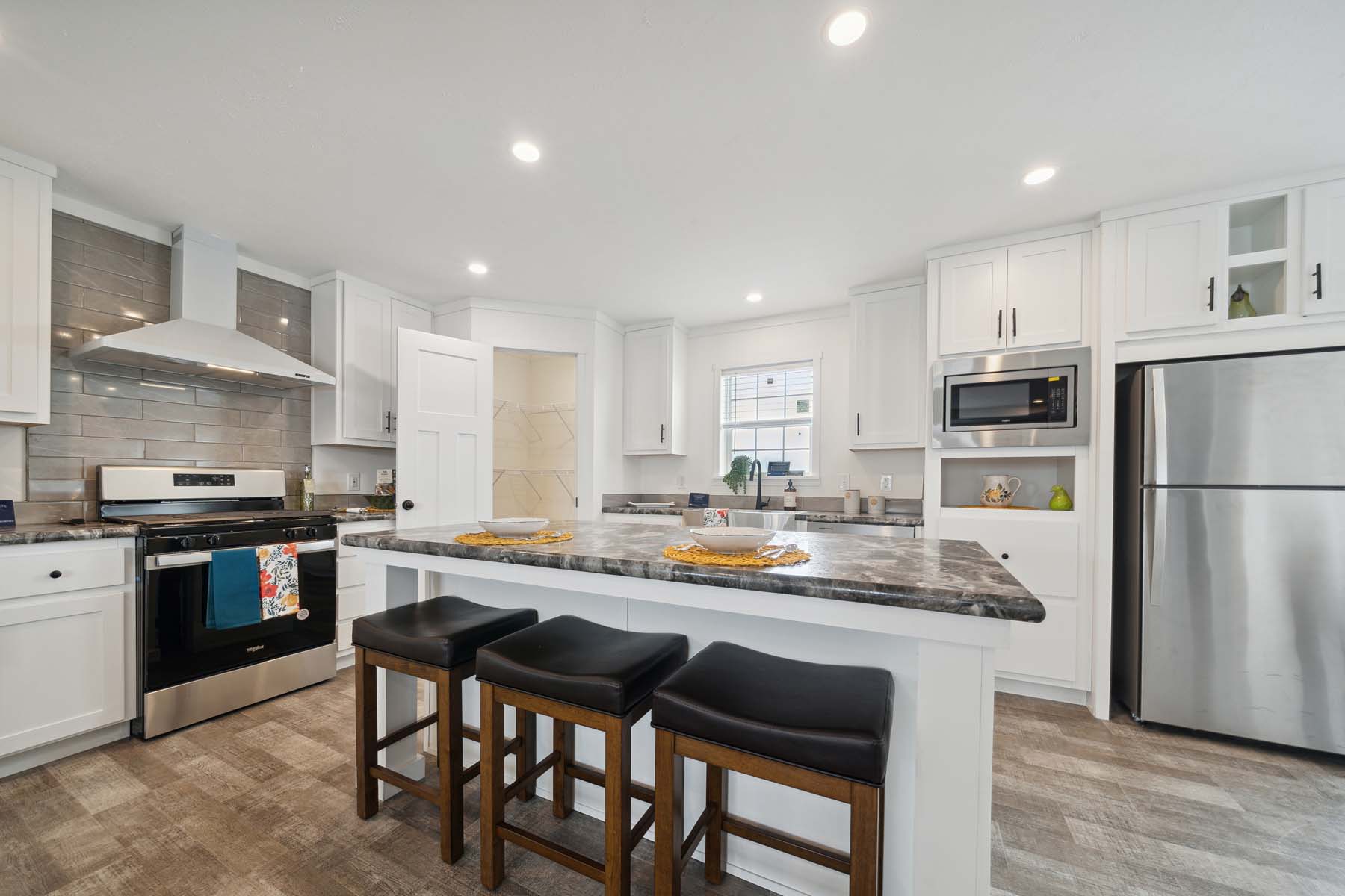 Modern kitchen with white cabinets, marble countertops, and stainless steel appliances. Center island with three stools creates a cozy, inviting space.