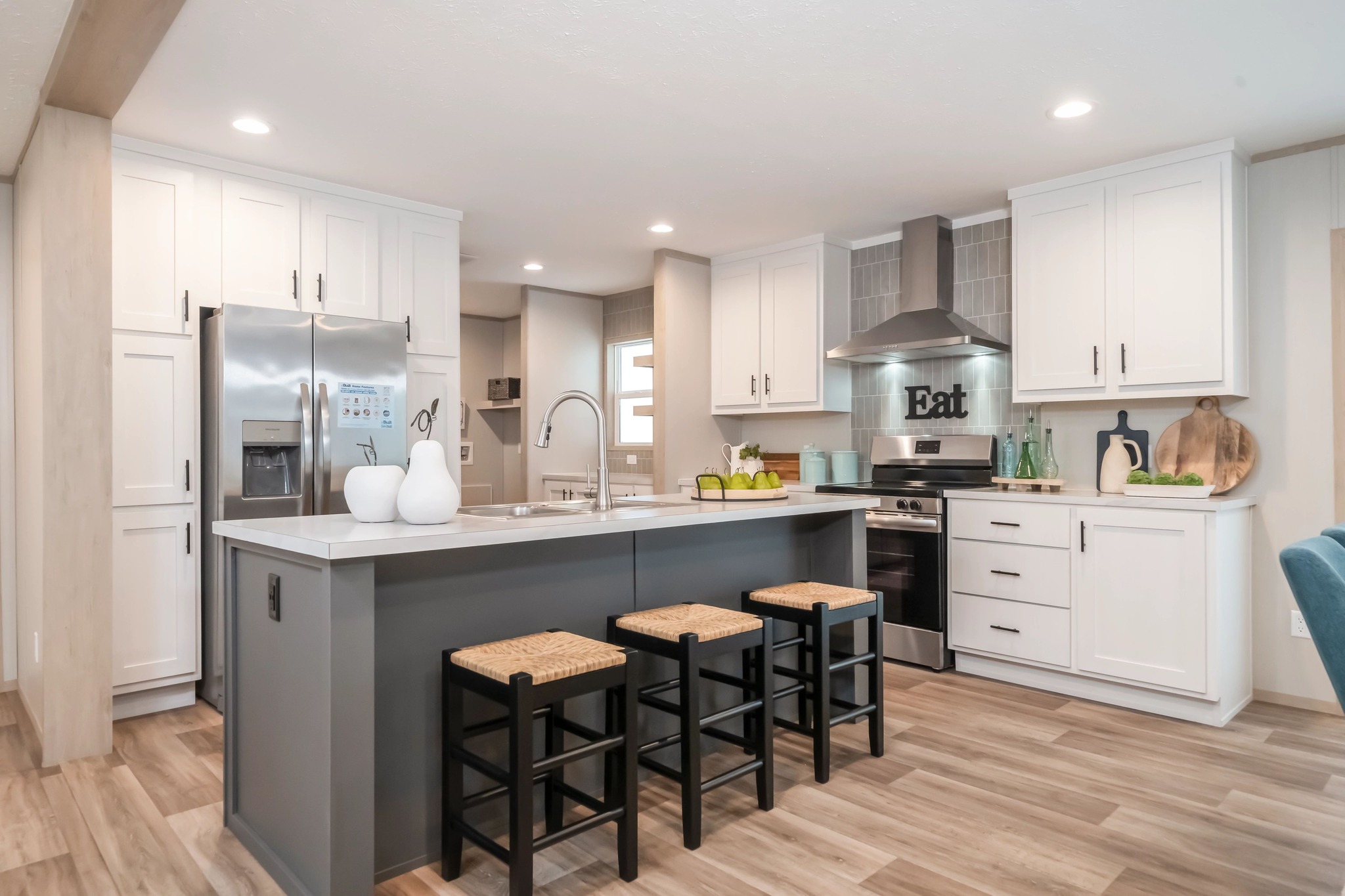 Modern kitchen with white cabinets, stainless steel appliances, and a large island with three stools. Bright, inviting atmosphere with decorative accents.
