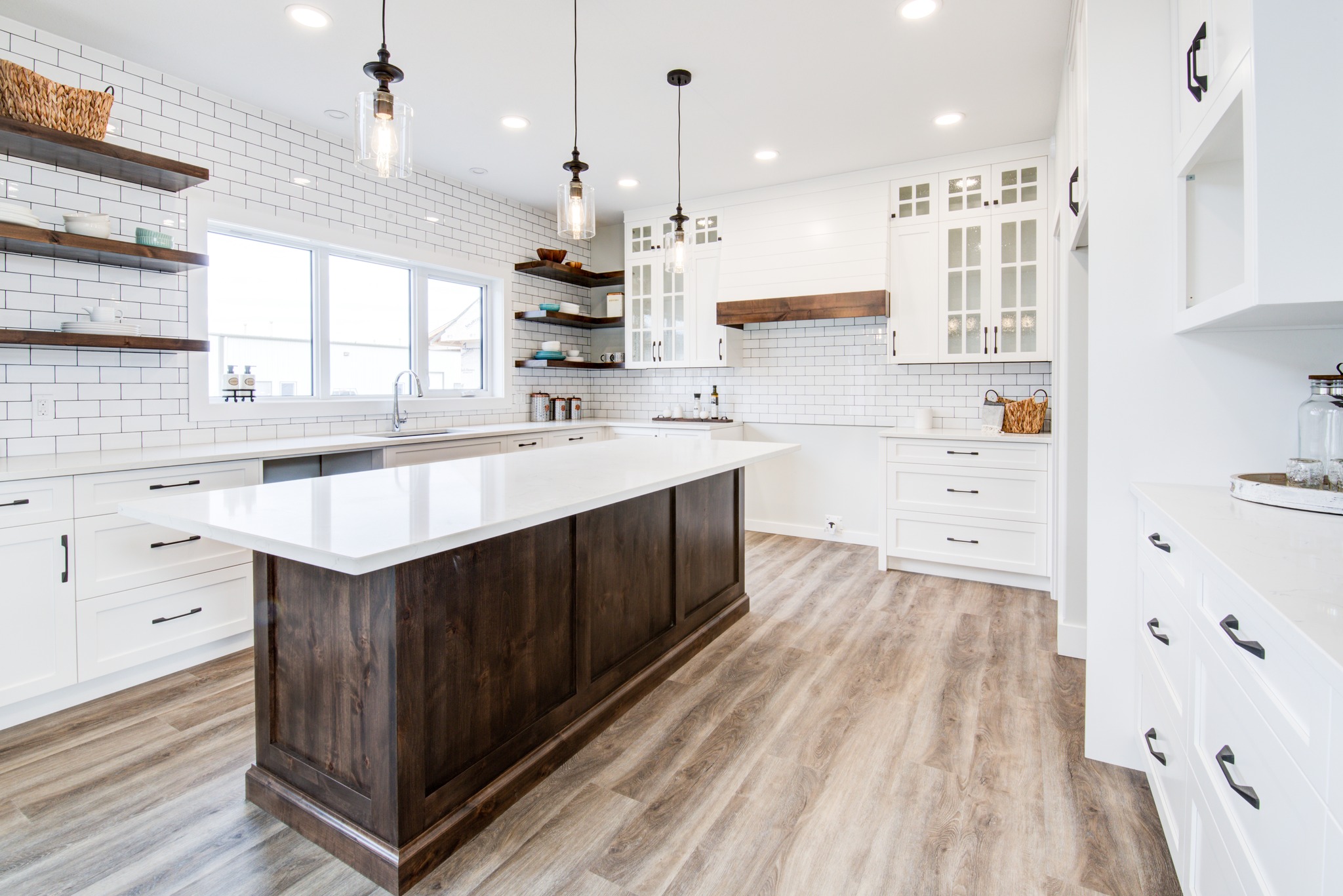 Spacious modern kitchen with white cabinets, large wooden island, and pendant lights. Bright, airy feel with white brick backsplash and wooden floors.