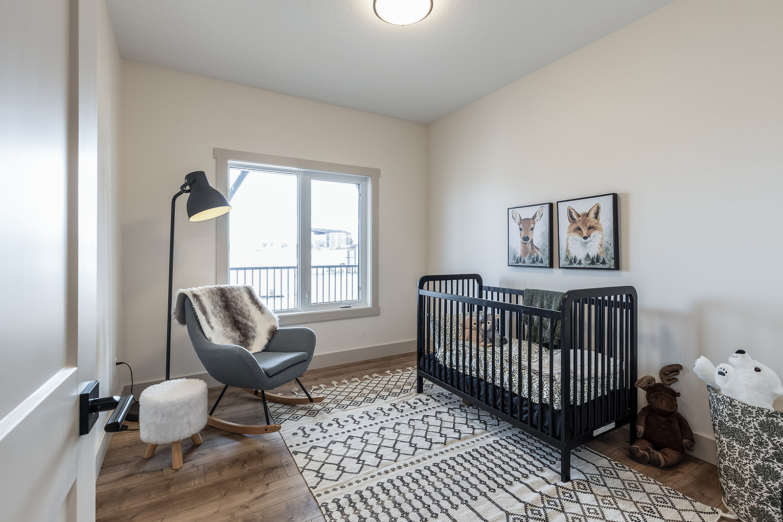 A cozy nursery with a black crib, animal-themed wall art, a gray rocking chair, and floor lamp. Neutral tones create a calm, inviting atmosphere.