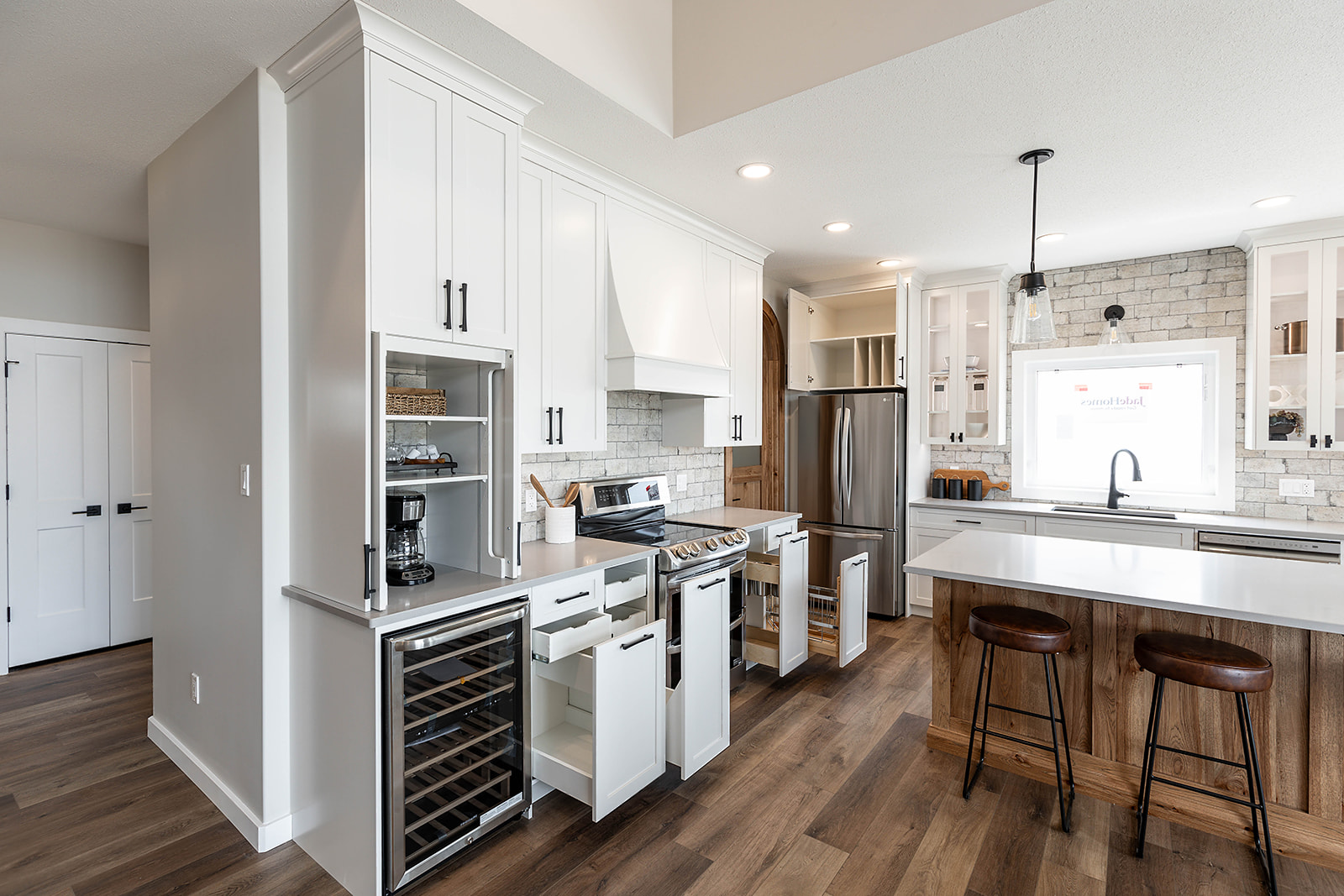 Modern kitchen with white cabinets and stainless steel appliances. Cabinets are open, showing storage and organization. Bright, with wood floors and pendant lighting, creating a sleek, inviting atmosphere.
