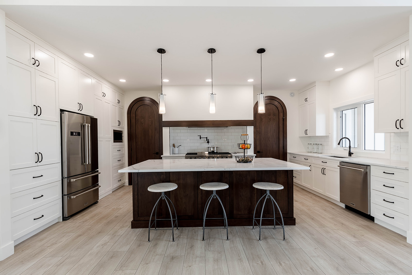 Modern kitchen with white cabinets, stainless steel appliances, and a large dark wood island. Three pendant lights hang above silver stools.