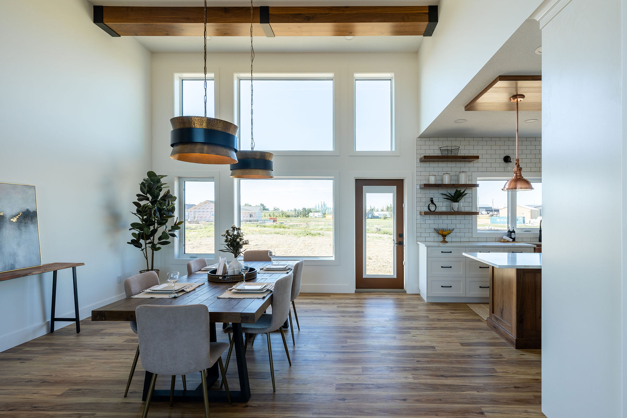 Spacious dining room with high ceilings, large windows, and wooden beams. A wooden table is set for six. Light, airy ambiance with modern decor.