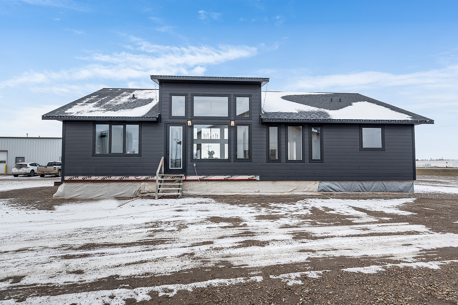 Modern grey house with large windows and a snowy front yard. Bright, clear sky in the background, suggesting a crisp, cold day.