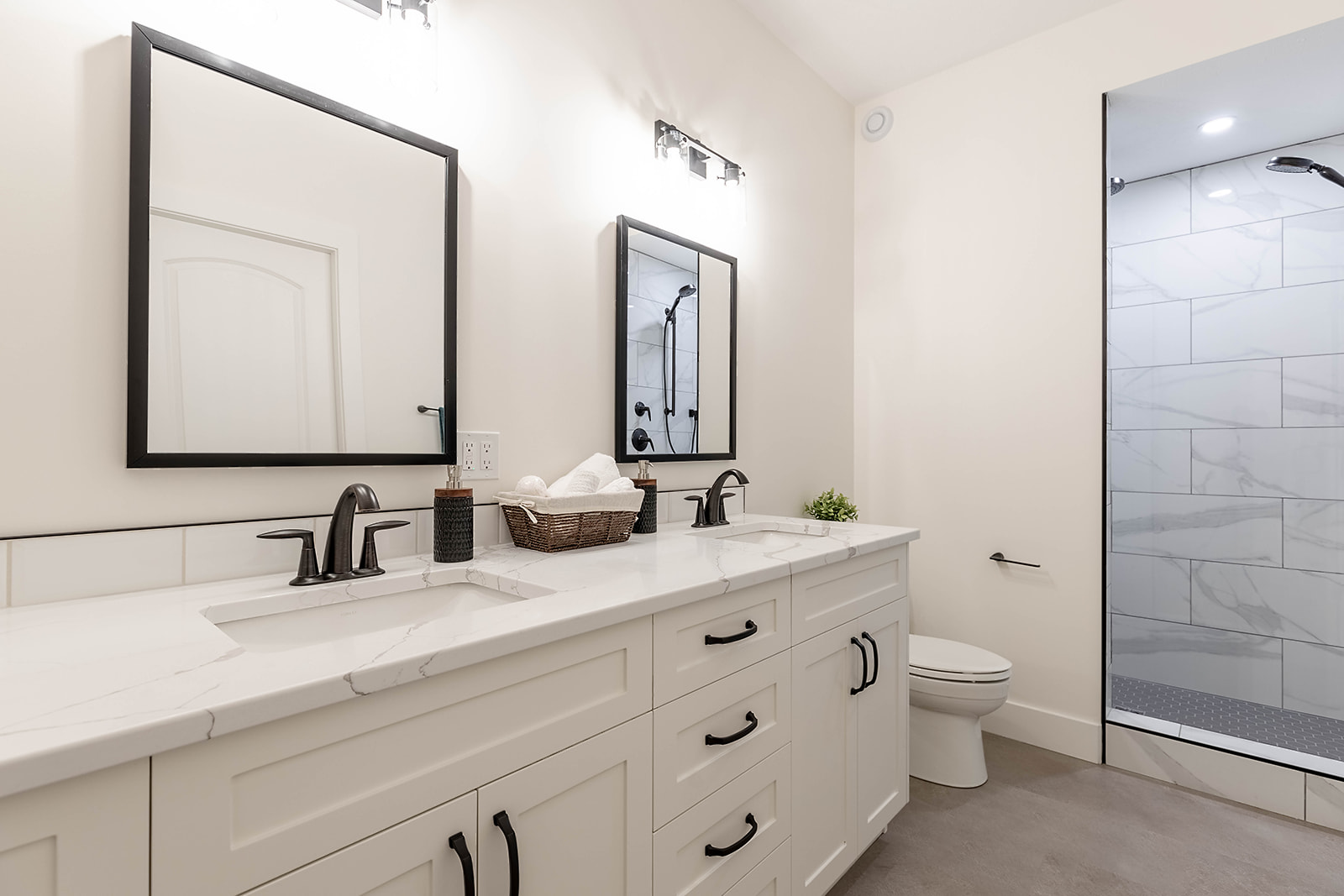 Modern bathroom with white double vanity, marble countertop, black fixtures, two mirrors, and a walk-in shower. Soft, inviting lighting sets a clean tone.