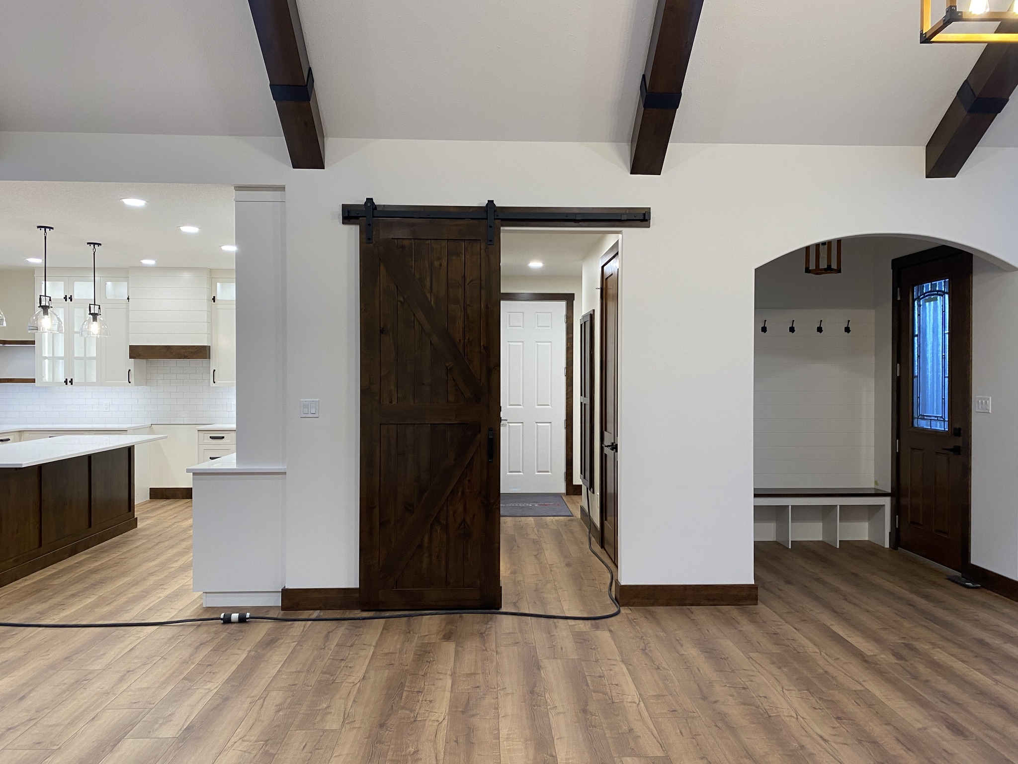 Spacious interior featuring a rustic sliding barn door, white kitchen with pendant lights and wooden beams, and a cozy nook with hooks and bench.