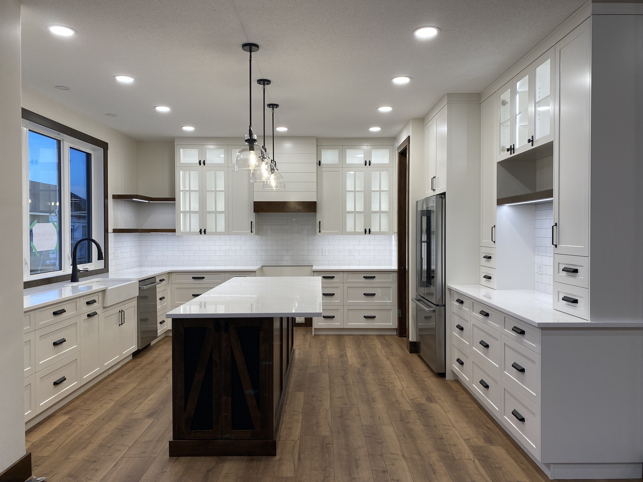 Spacious modern kitchen with white cabinets, wooden floors, and a central island. Pendant lights illuminate a sleek, elegant, and inviting space.