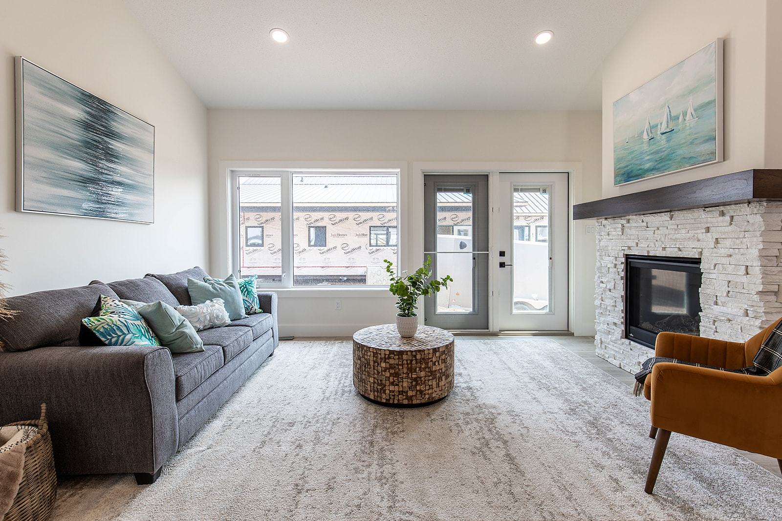A modern living room with a gray sofa adorned with teal and gray pillows, a mosaic round coffee table, brick fireplace, and nautical-themed art, exuding a cozy, serene atmosphere.