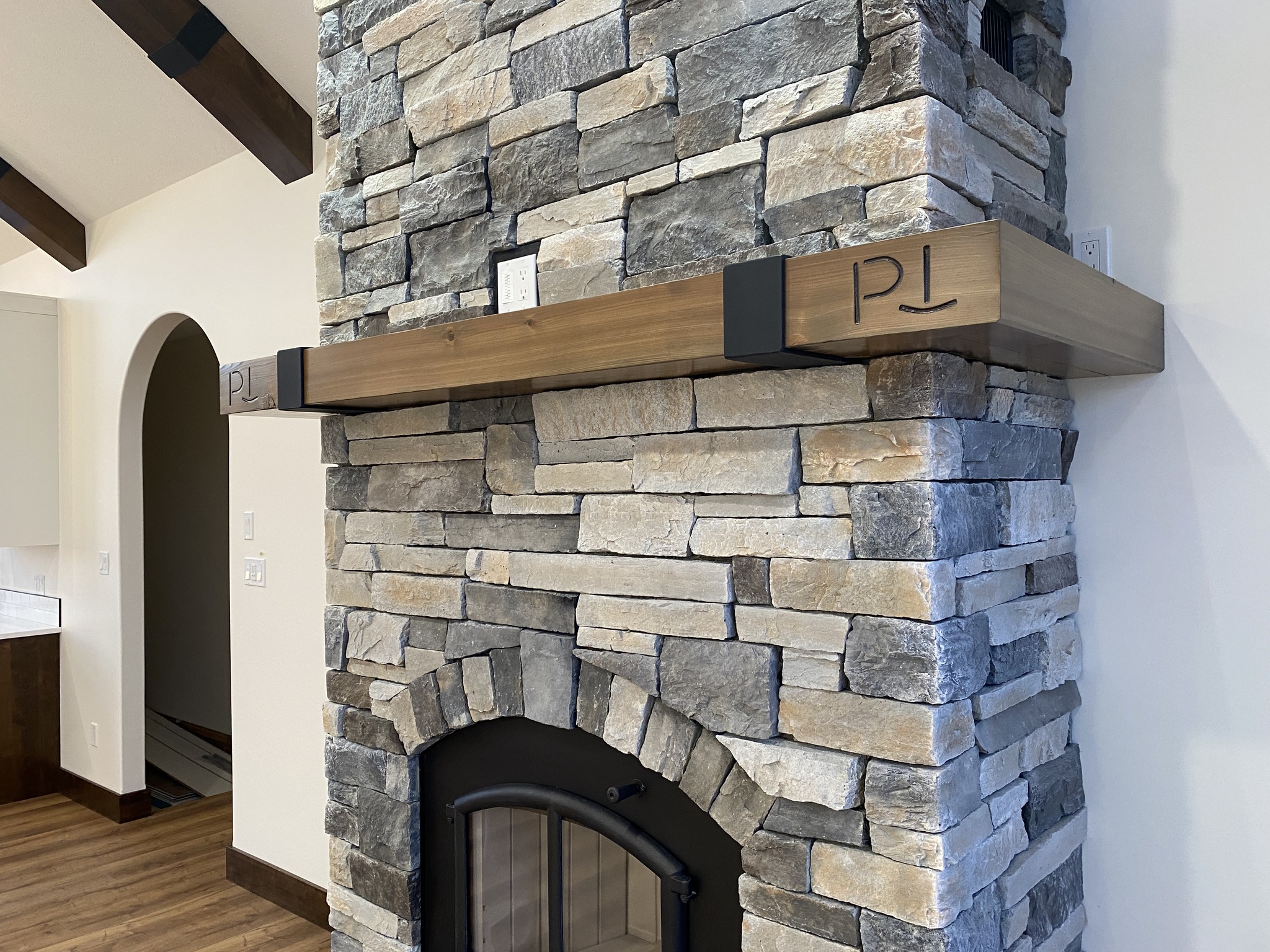 Rustic stone fireplace with a wooden mantel featuring a carved symbol. The room has wooden beams and a warm, inviting tone.