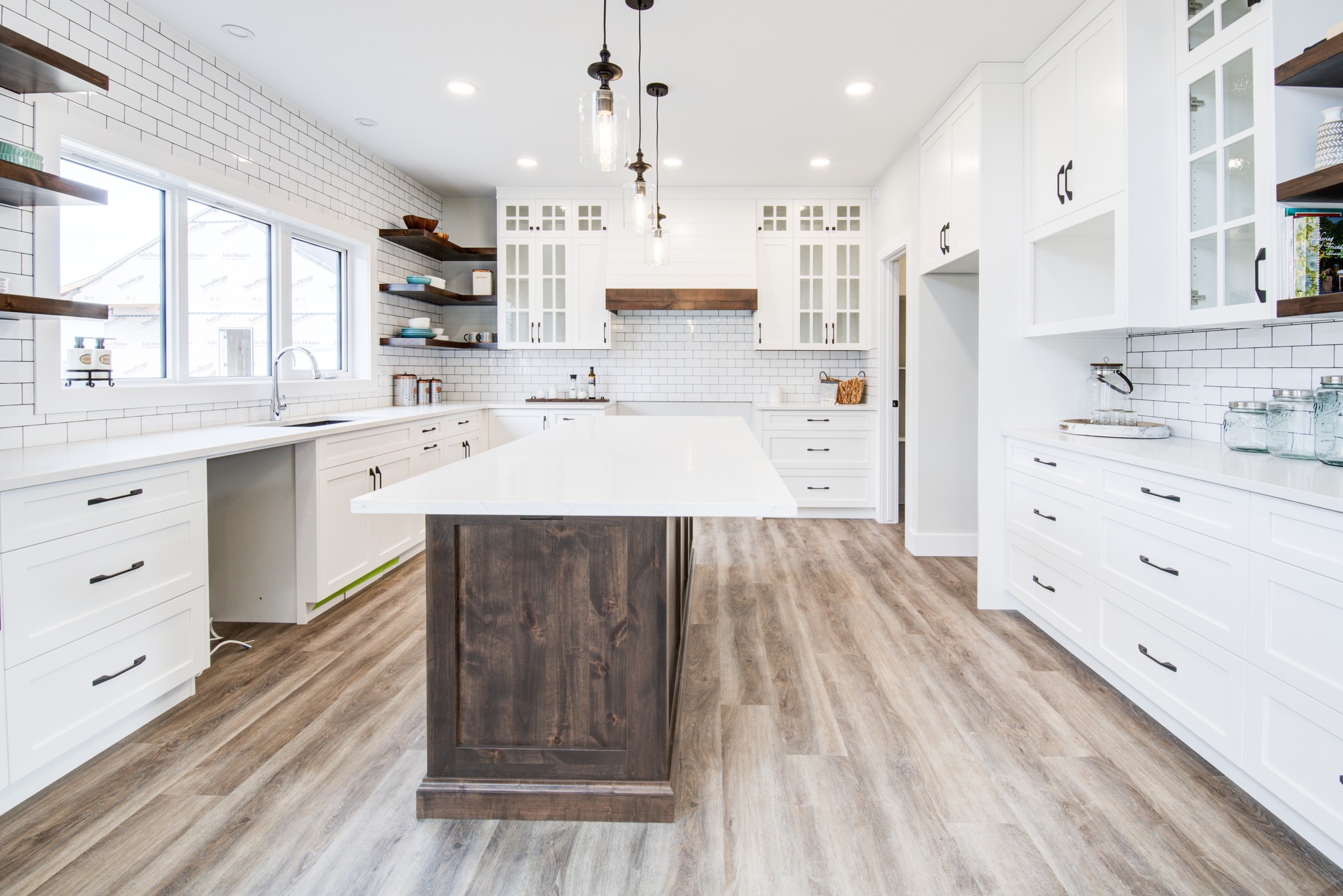 Spacious modern kitchen with white cabinetry, a large dark wood island, and light wood flooring. Pendant lights hang from the ceiling. Bright, clean atmosphere.
