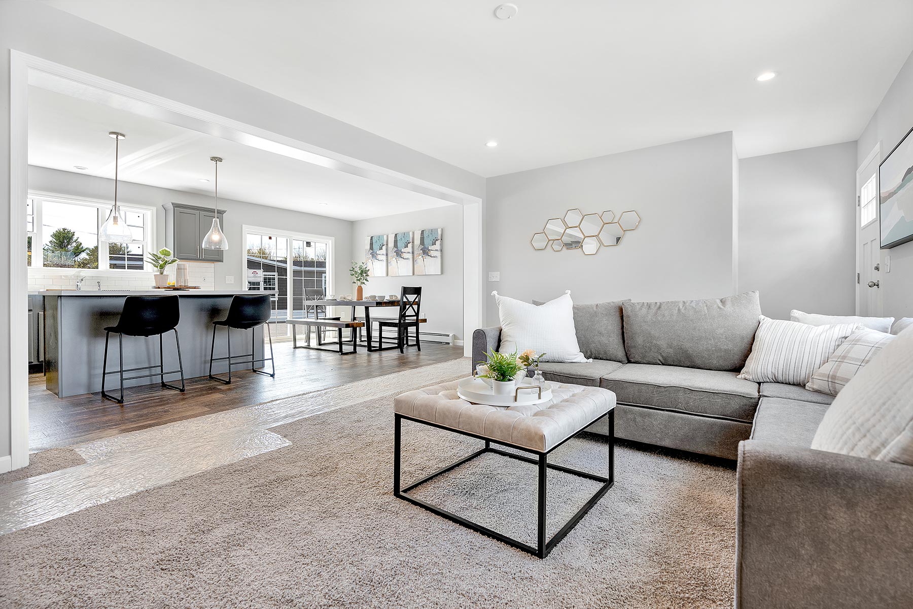 Modern living area with gray sectional sofa and decorative pillows, adjacent to a dining area with a table and black chairs. Bright, airy, and inviting ambiance.