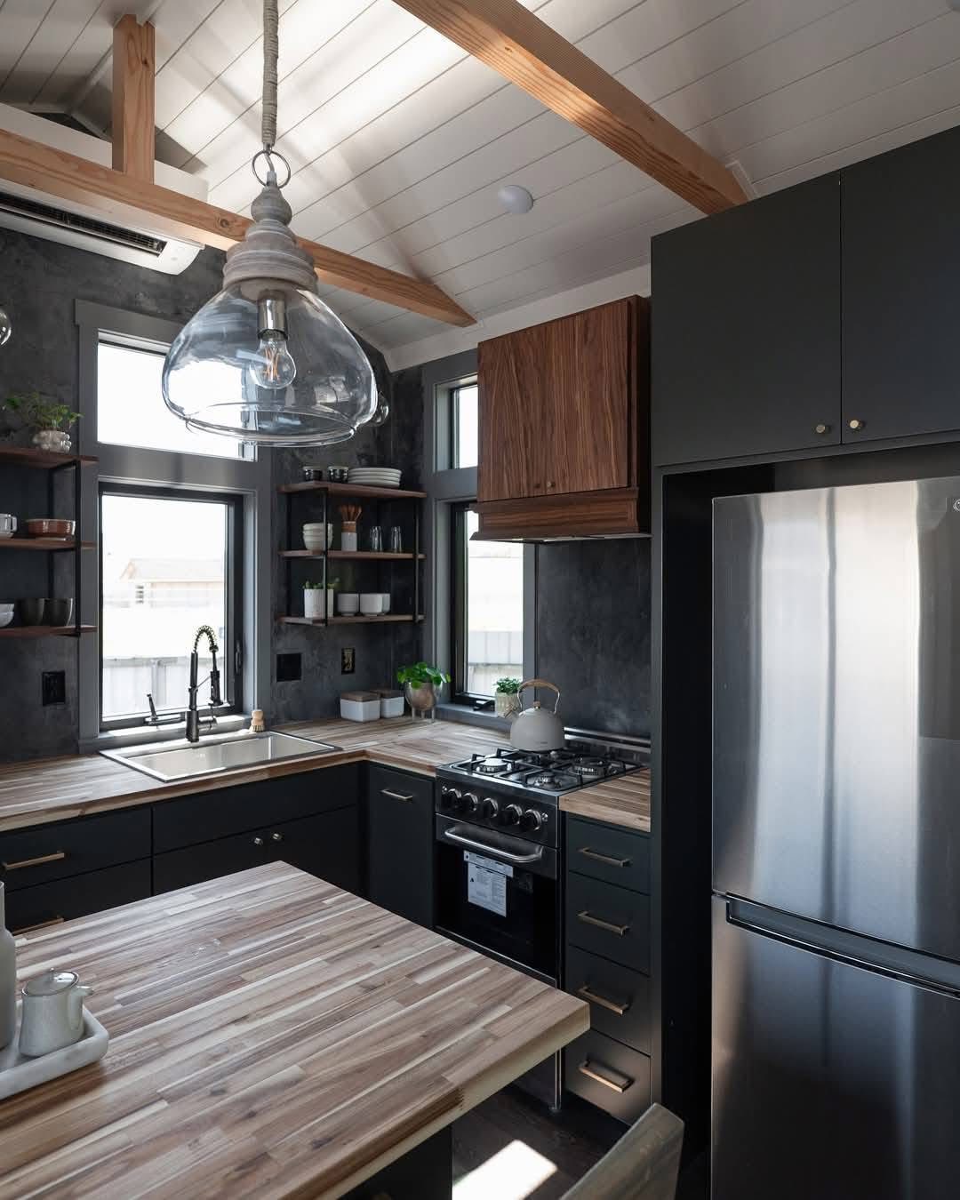 Modern kitchen with wooden countertops, dark cabinetry, and stainless steel appliances. A large glass pendant light and open shelving enhance the space.