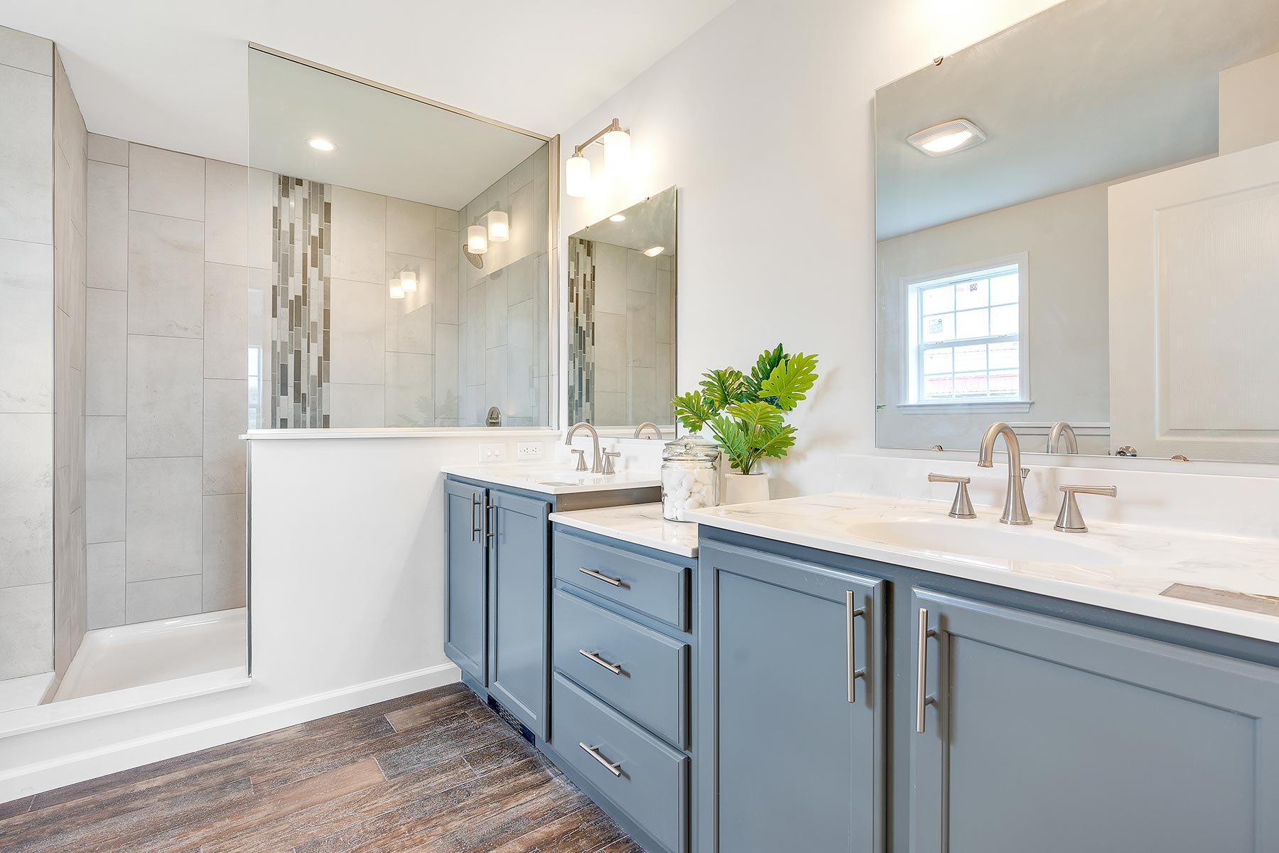 Elegant bathroom with double vanity in light blue, modern fixtures, large mirrors, and a walk-in shower. Bright, clean, and contemporary design.