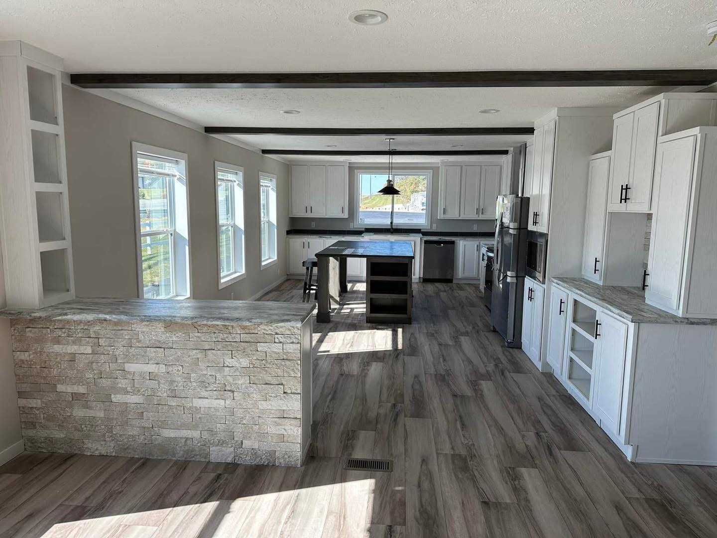 Spacious modern kitchen with light wood flooring, white cabinets, and black accents. Features an island with stools, ample natural light from large windows.