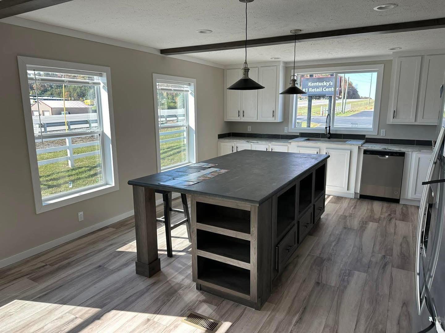 Bright modern kitchen with two large windows and an island. Light wood floors contrast with dark countertops and white cabinetry, creating a welcoming space.