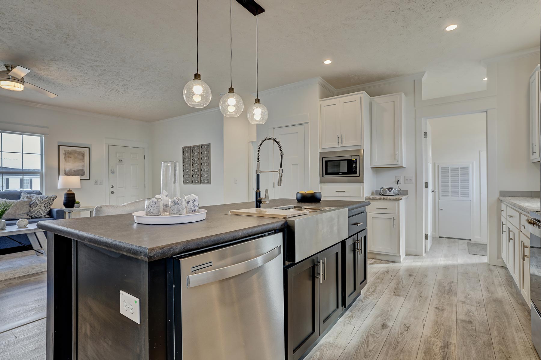 Modern kitchen with pendant lights over island featuring a stainless-steel dishwasher. Bright, airy space with white cabinets and wood flooring.