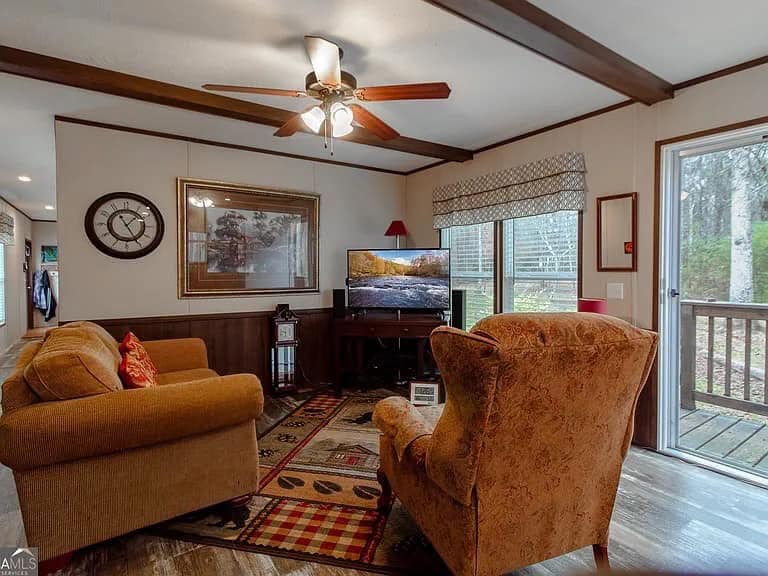 Cozy living room with two soft armchairs, patterned rug, and TV near a sliding glass door. Warm lighting and rustic decor create a welcoming atmosphere.