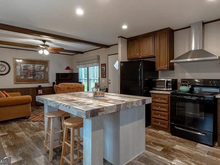 Modern kitchen and living area with a rustic vibe. Features a wooden island with stools, dark appliances, warm lighting, and cozy seating area.