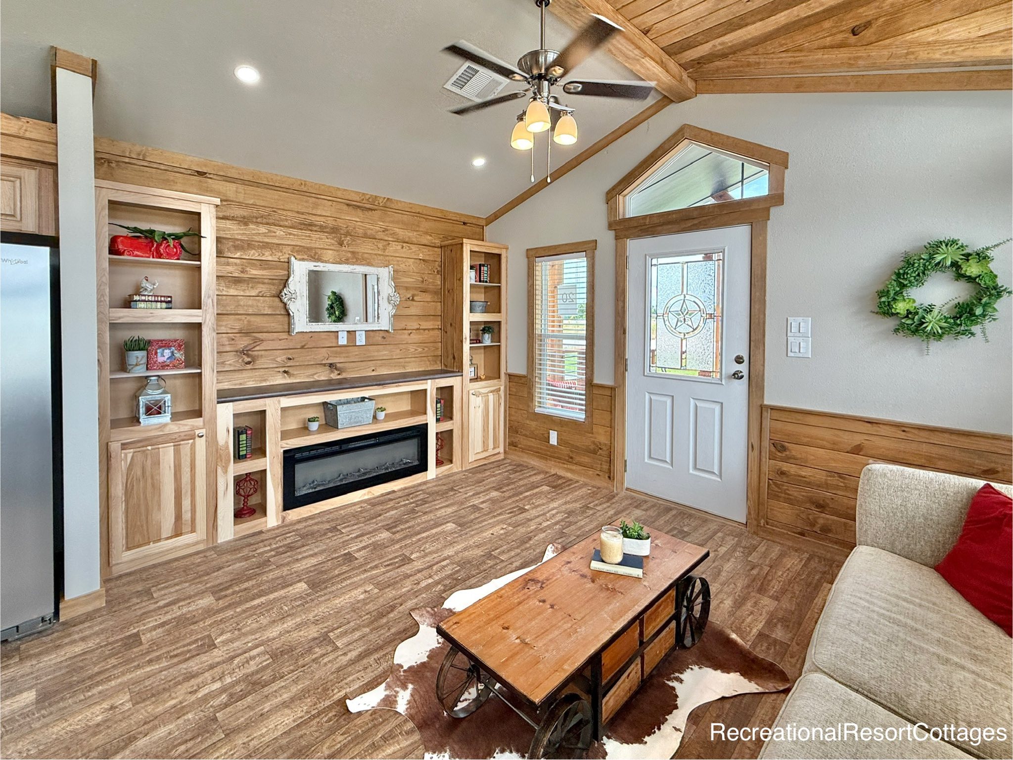 Cozy living room with rustic wood walls, a fireplace, and built-in shelves. A wagon-style table on a cowhide rug complements the warm decor.