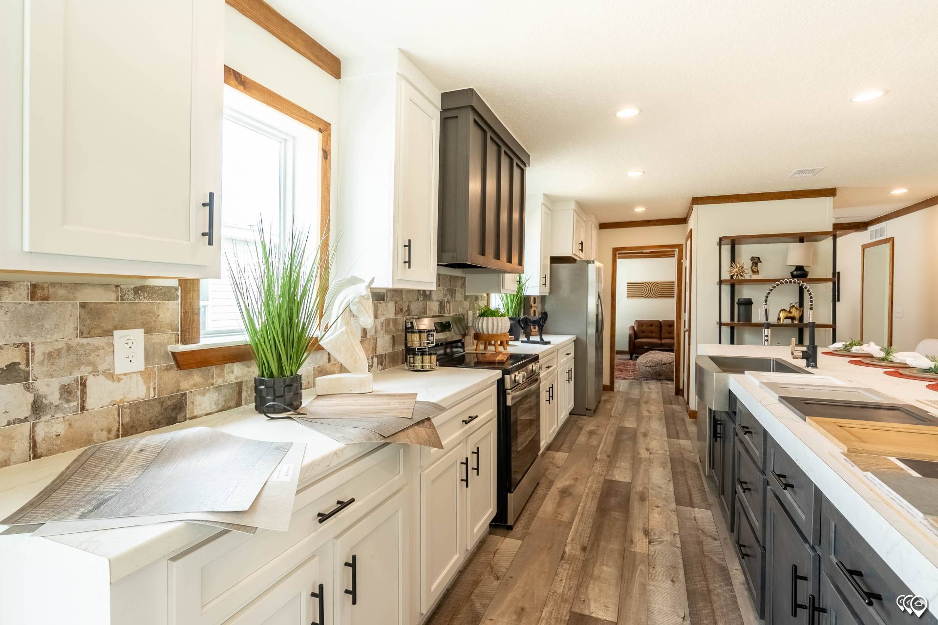 A bright, modern kitchen with white and dark cabinets, wood accents, stone backsplash, and light wood floors. Sleek decor and green plants add freshness.