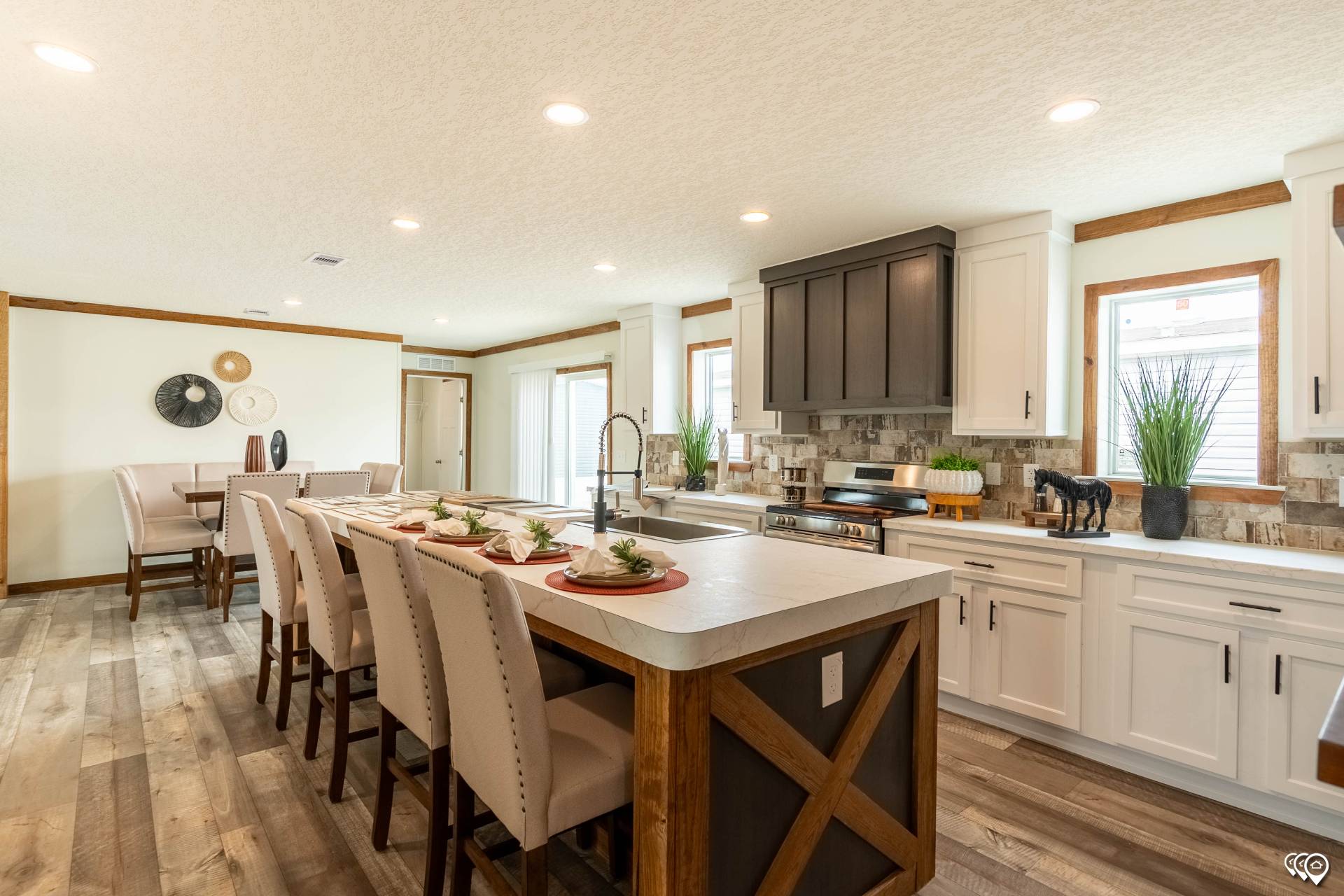Spacious kitchen with a large island, high chairs, and modern decor. Bright lighting, wood accents, and potted plants create a warm, inviting atmosphere.