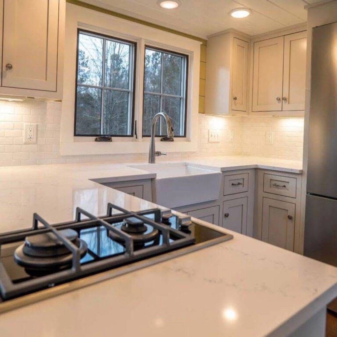 Modern kitchen with white cabinetry, marble countertops, and a farmhouse sink. A stainless steel stove and fridge create a sleek, minimalist vibe.