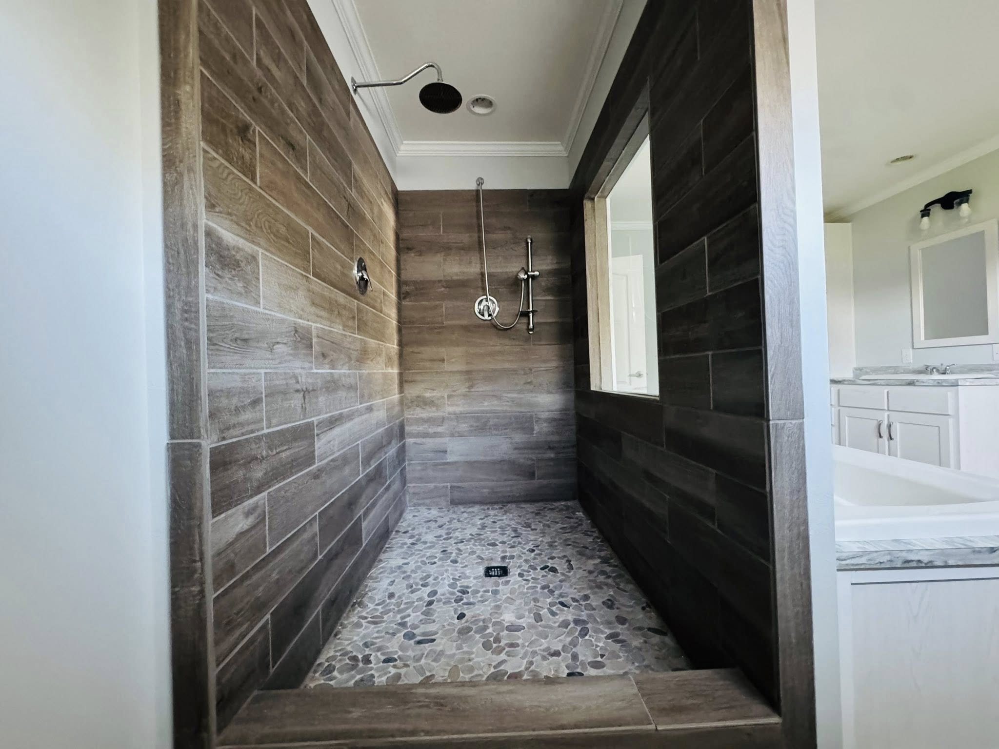 Spacious walk-in closet with white shelving, drawers, and hanging rods on gray walls. Sunlight filters through a window with blinds, illuminating wood-patterned floor.