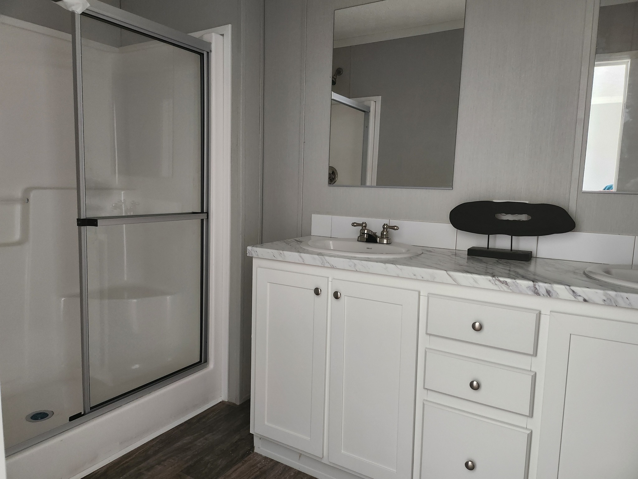 Modern bathroom with a glass-enclosed shower and a white vanity featuring a marble countertop and dual sinks. The atmosphere is clean and minimalistic.