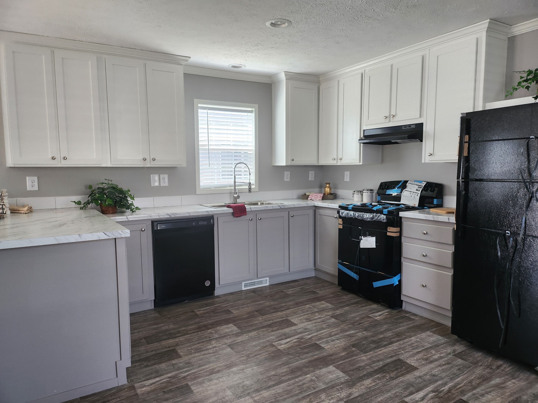 Modern kitchen with white cabinets, a black fridge, and a stove. Light pours in through a window above the sink, creating a cozy atmosphere.