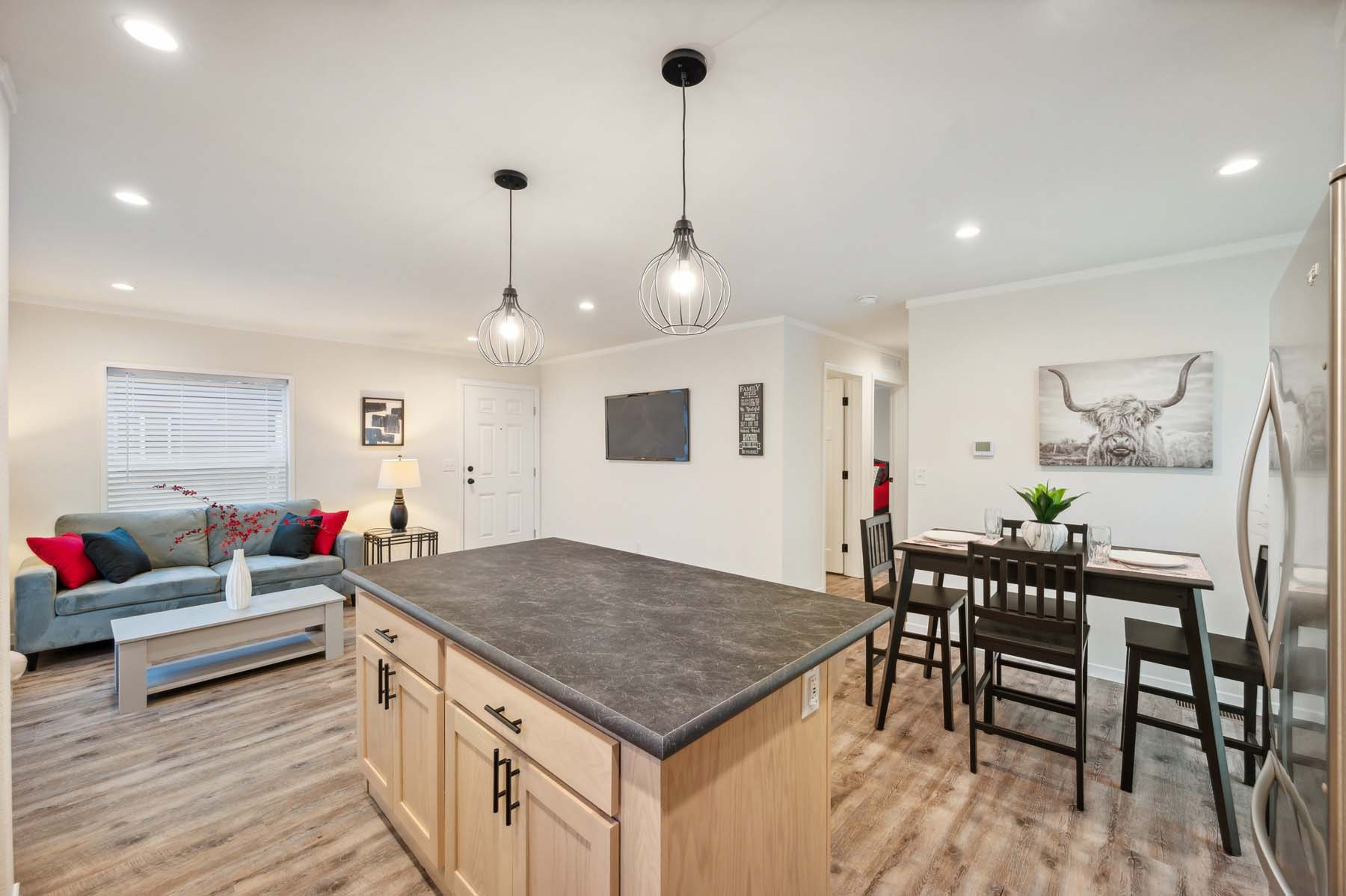 Modern open-plan kitchen and living area with wood flooring and neutral tones. Features a center island, cozy seating, and a dining table, conveying warmth.