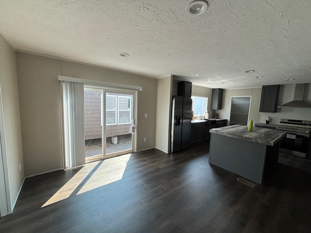 A modern kitchen with dark wood flooring, a central island with gray marble countertop, and stainless steel appliances. Sunlight streams through sliding glass doors.